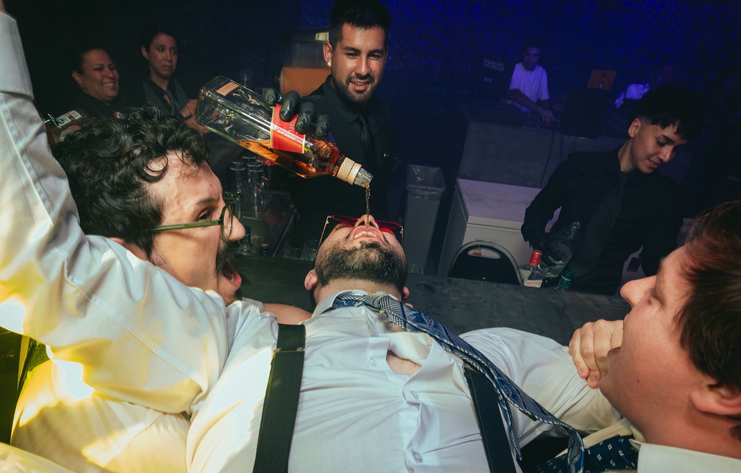 Wedding guest lying back receiving a drink pour at a lively reception party.