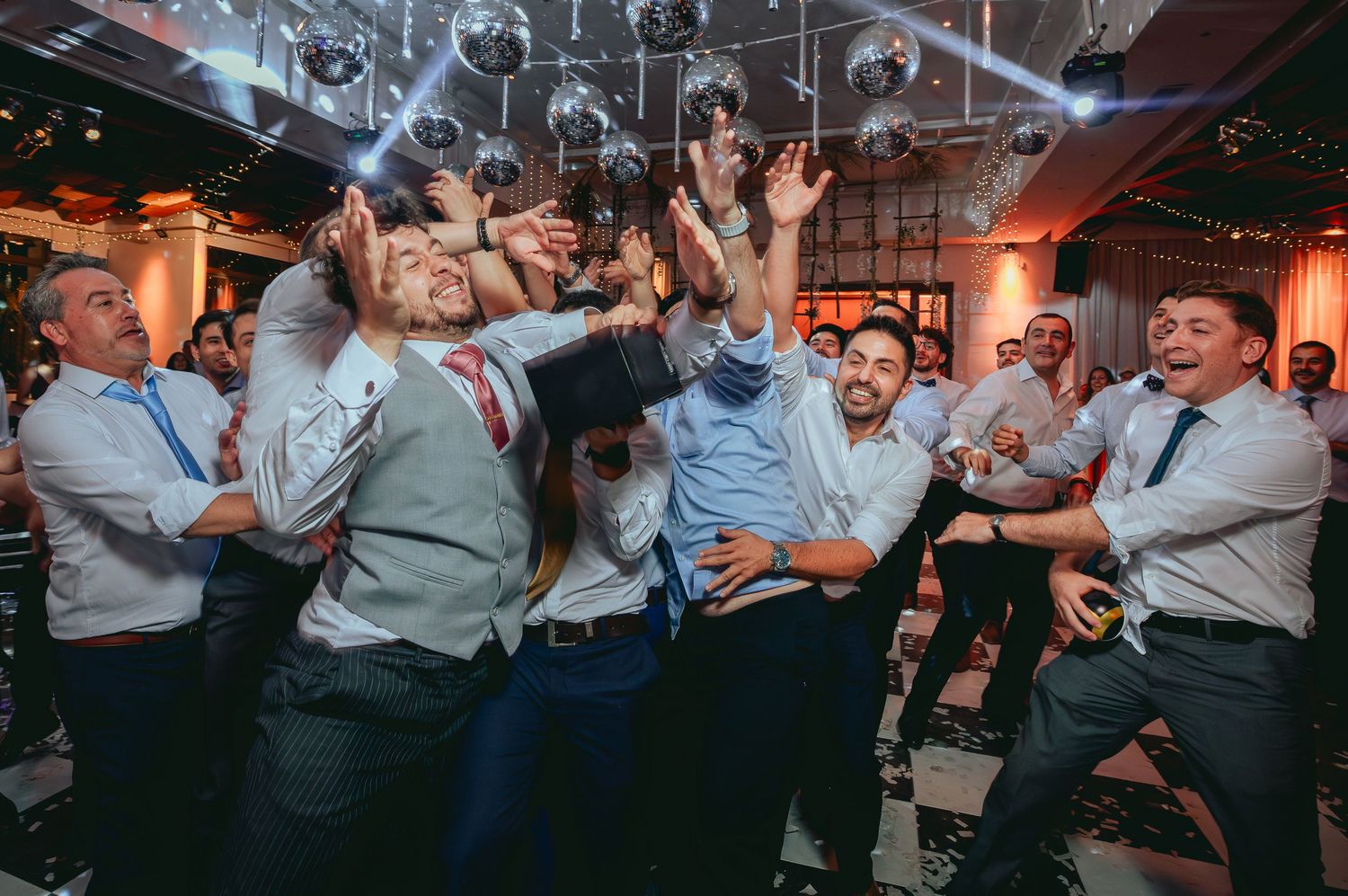 Wedding guests dancing and cheering enthusiastically under sparkling disco balls.