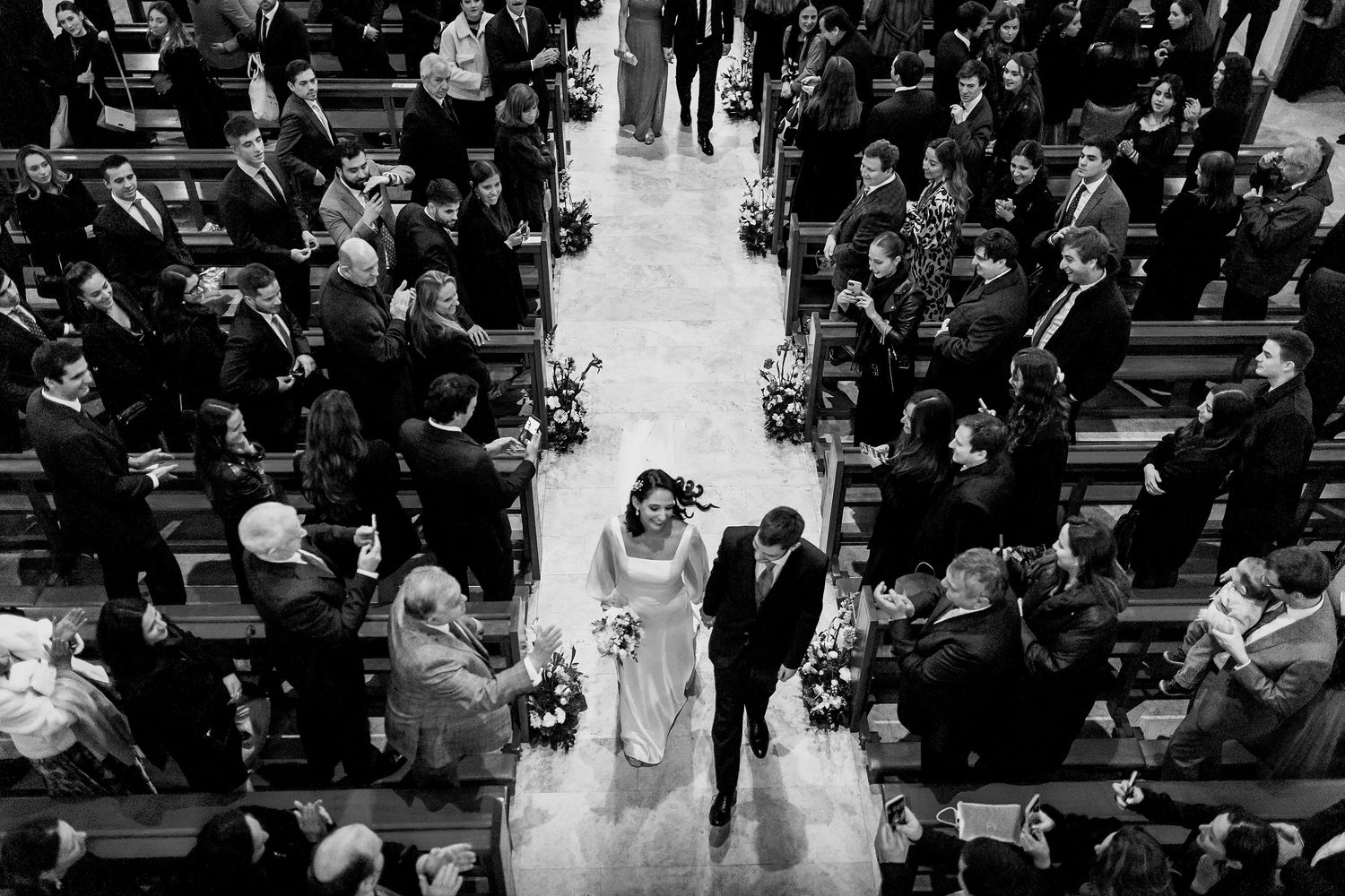 Aerial black and white photo of bride and groom walking down church aisle at wedding ceremony.
