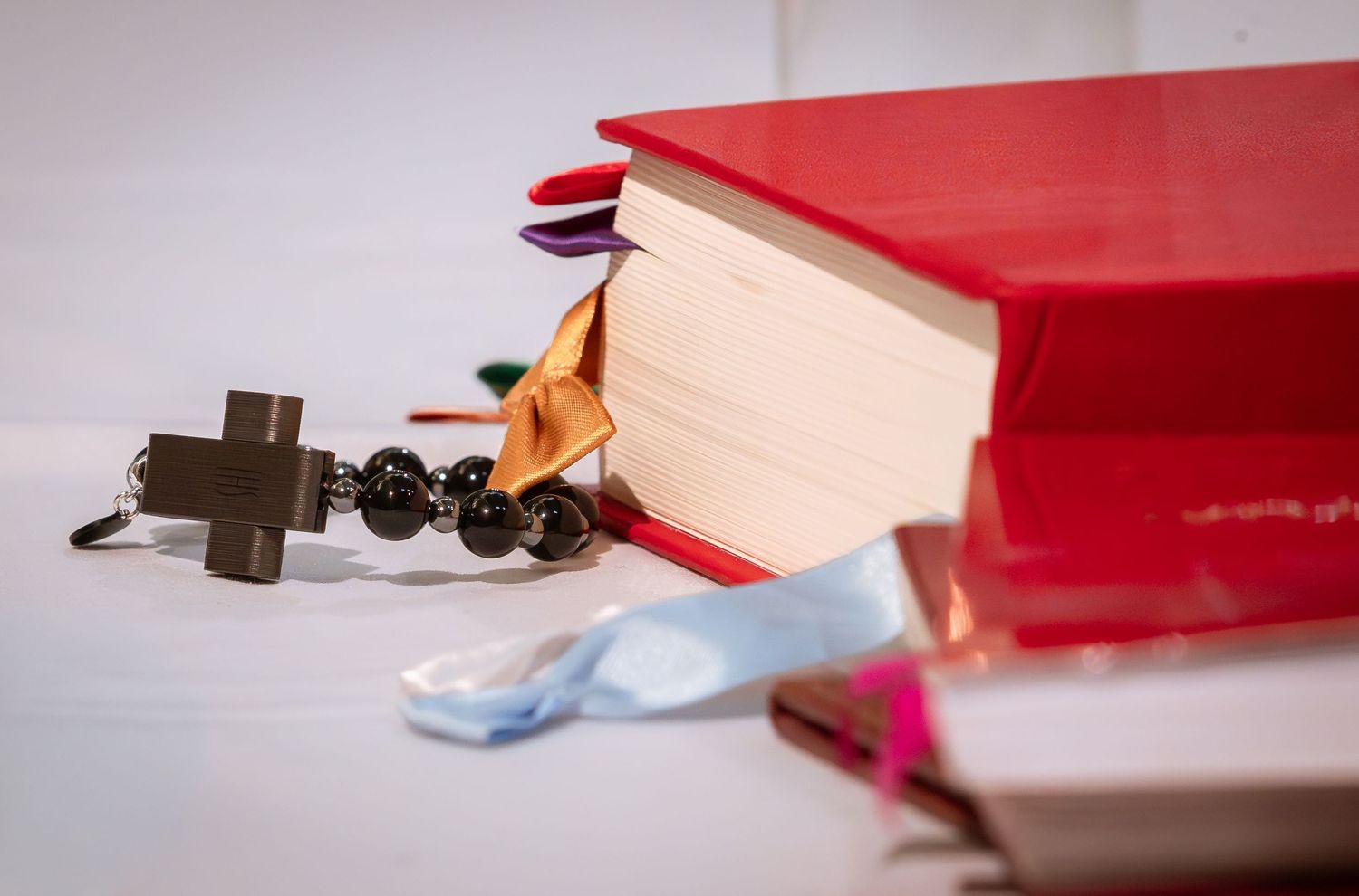 Red Catholic prayer books and rosary beads arranged on white surface for wedding ceremony.