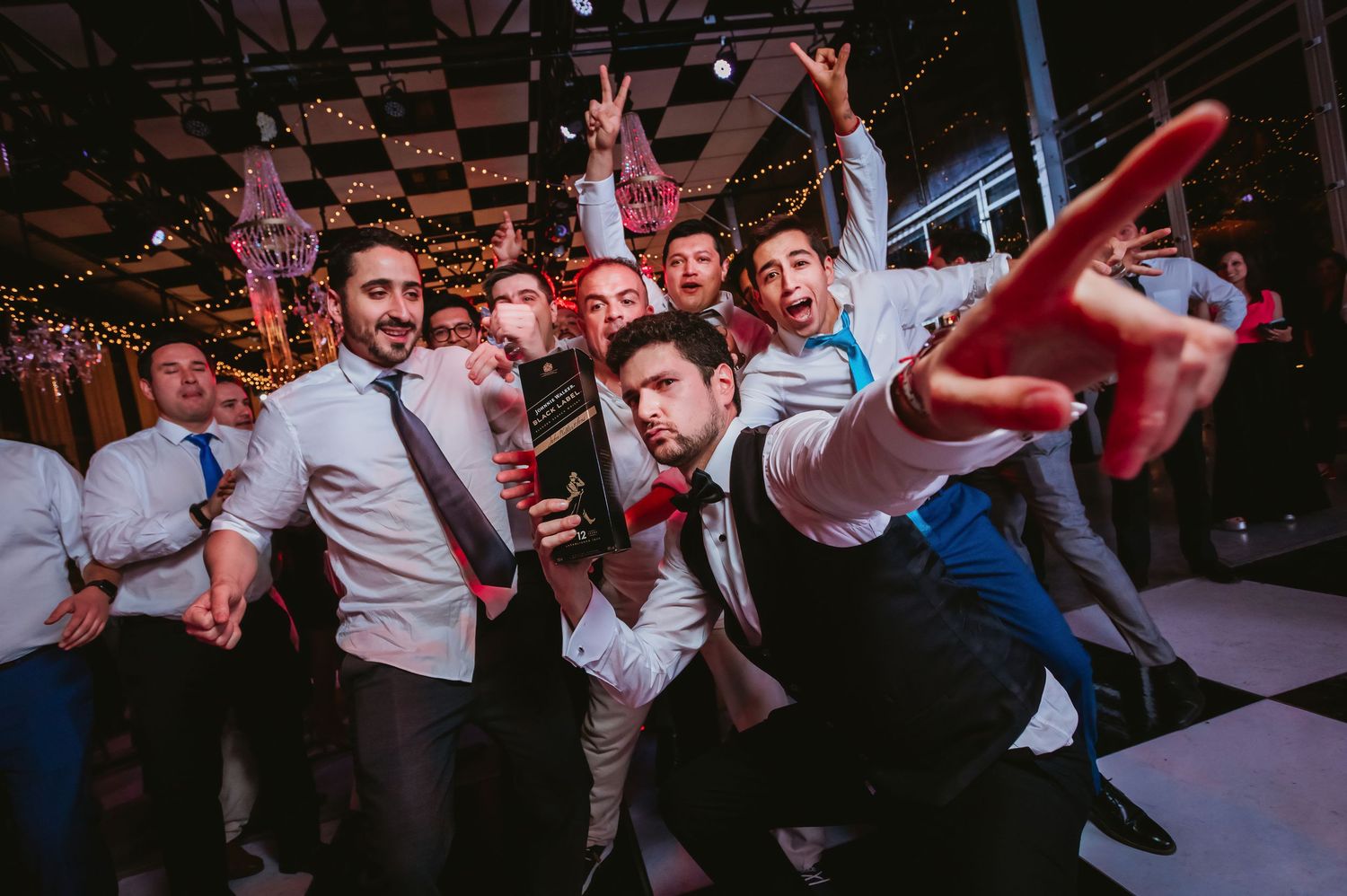 Group of men in dress shirts celebrating and posing energetically on a wedding dance floor.