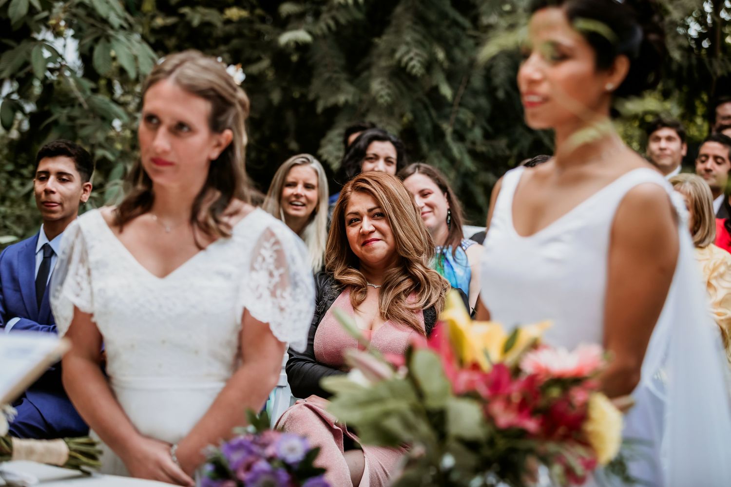 Emotional wedding guest watches two brides during an outdoor garden ceremony.