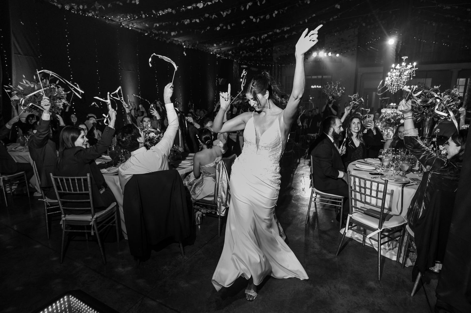 Bride dancing joyfully with guests at a wedding reception in black and white photography.