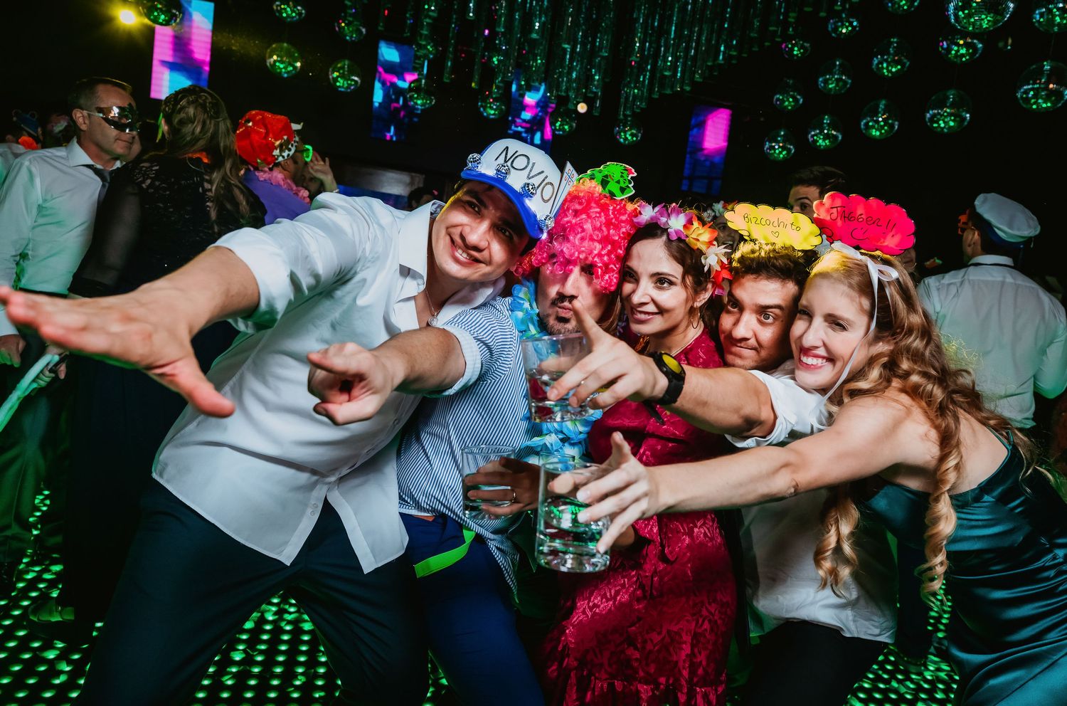 Happy group of friends toasting drinks and posing together at a colorful neon-lit party.