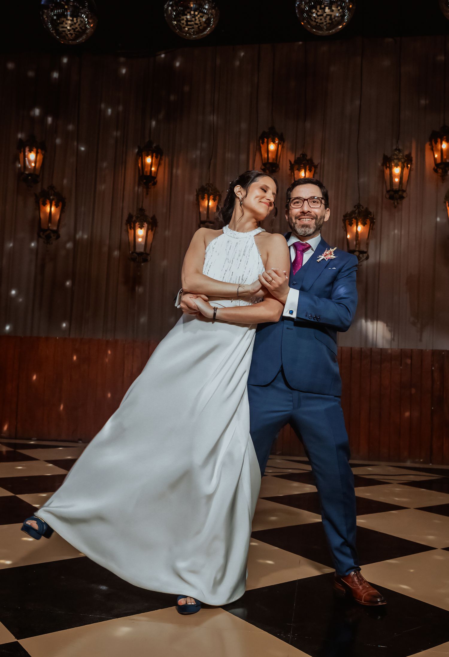 Bride and groom share romantic first dance on black and white checkered ballroom floor.