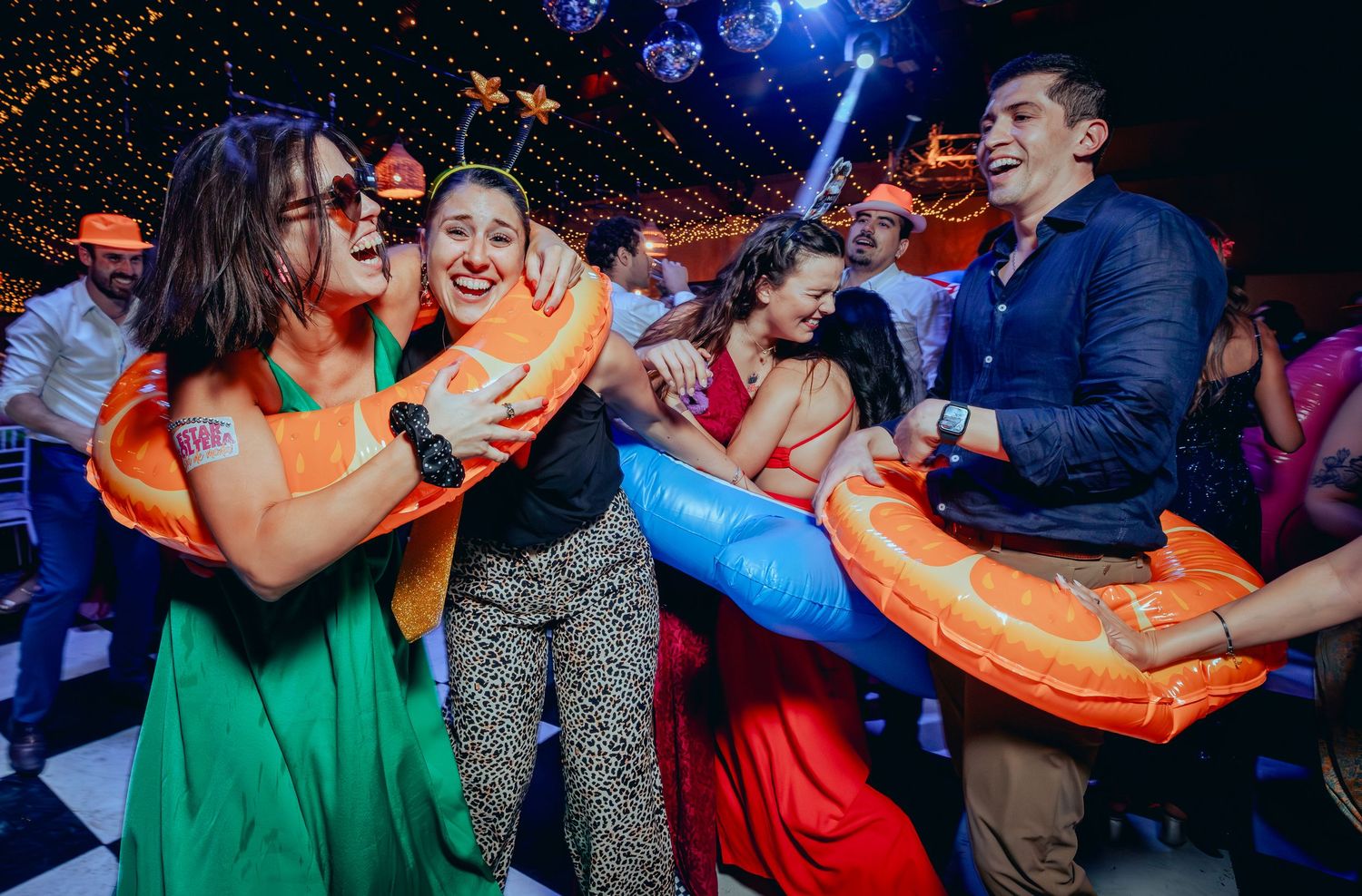 Wedding guests laughing and dancing with inflatable pool floats at a vibrant indoor reception party.