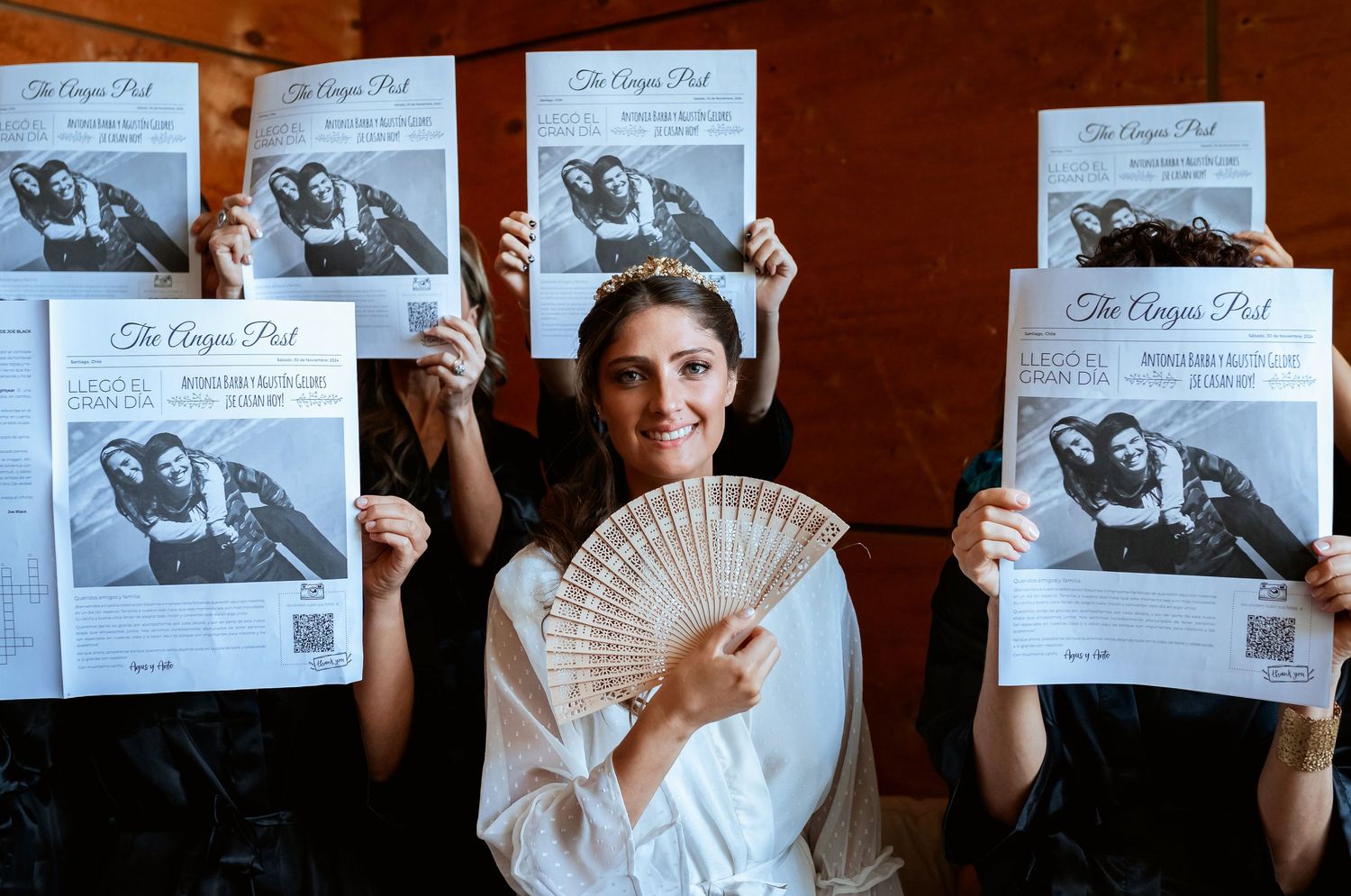 Bride holding a fan while bridesmaids hold up The Angus Post wedding newspapers behind her.
