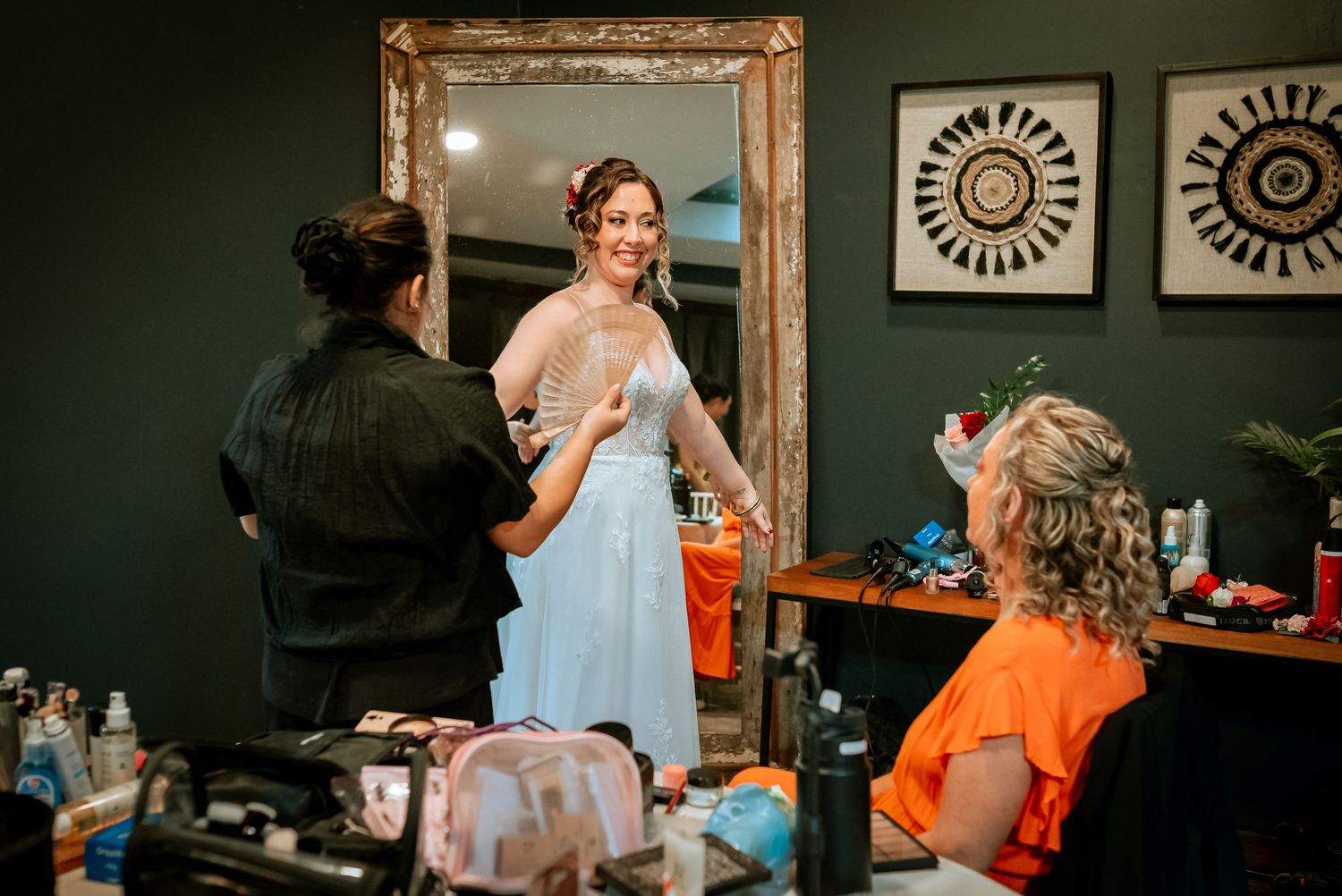 Bride in white gown gets ready with help from stylist in elegant dressing room before wedding.