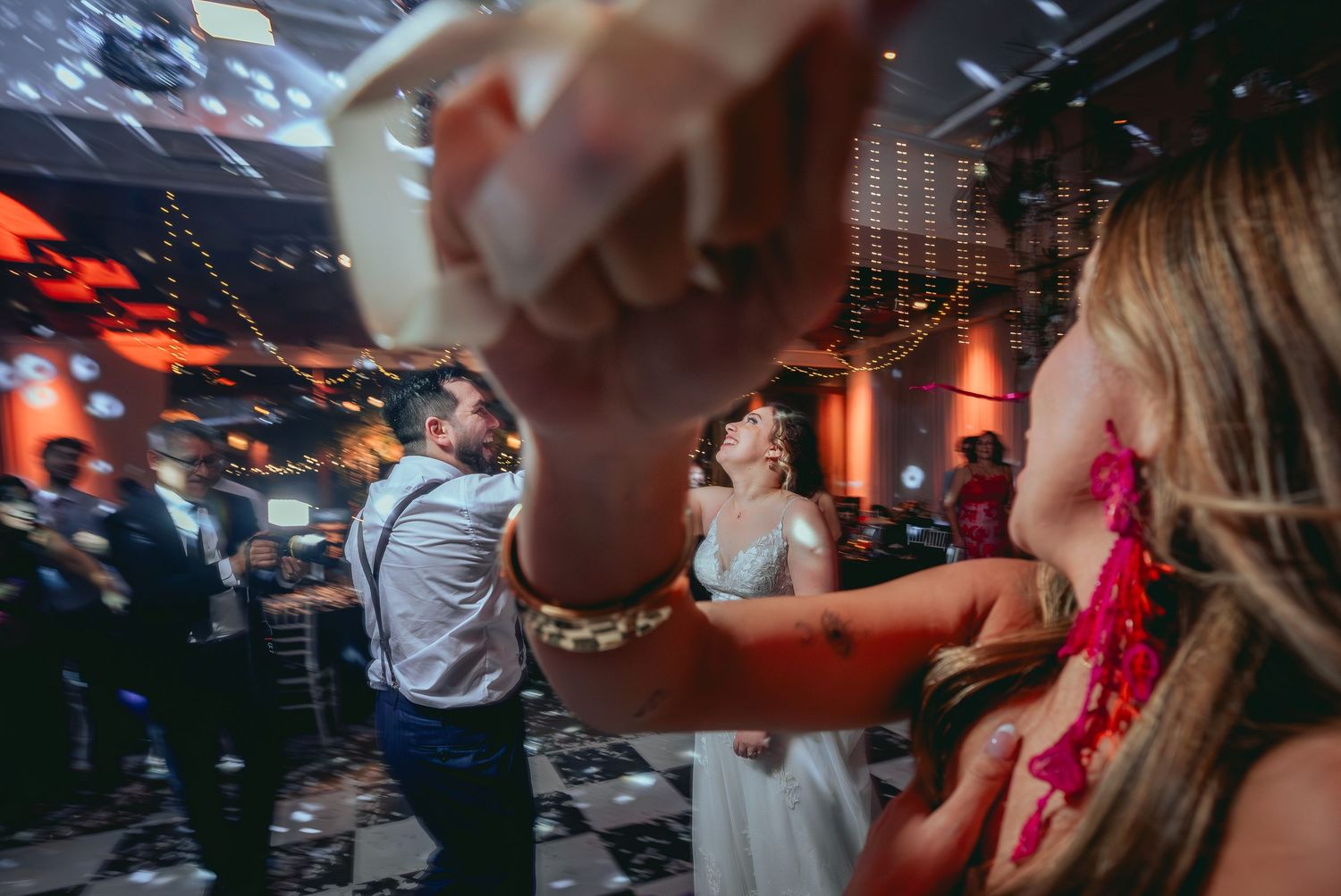Bride and groom dancing energetically with guests at lively wedding reception party.