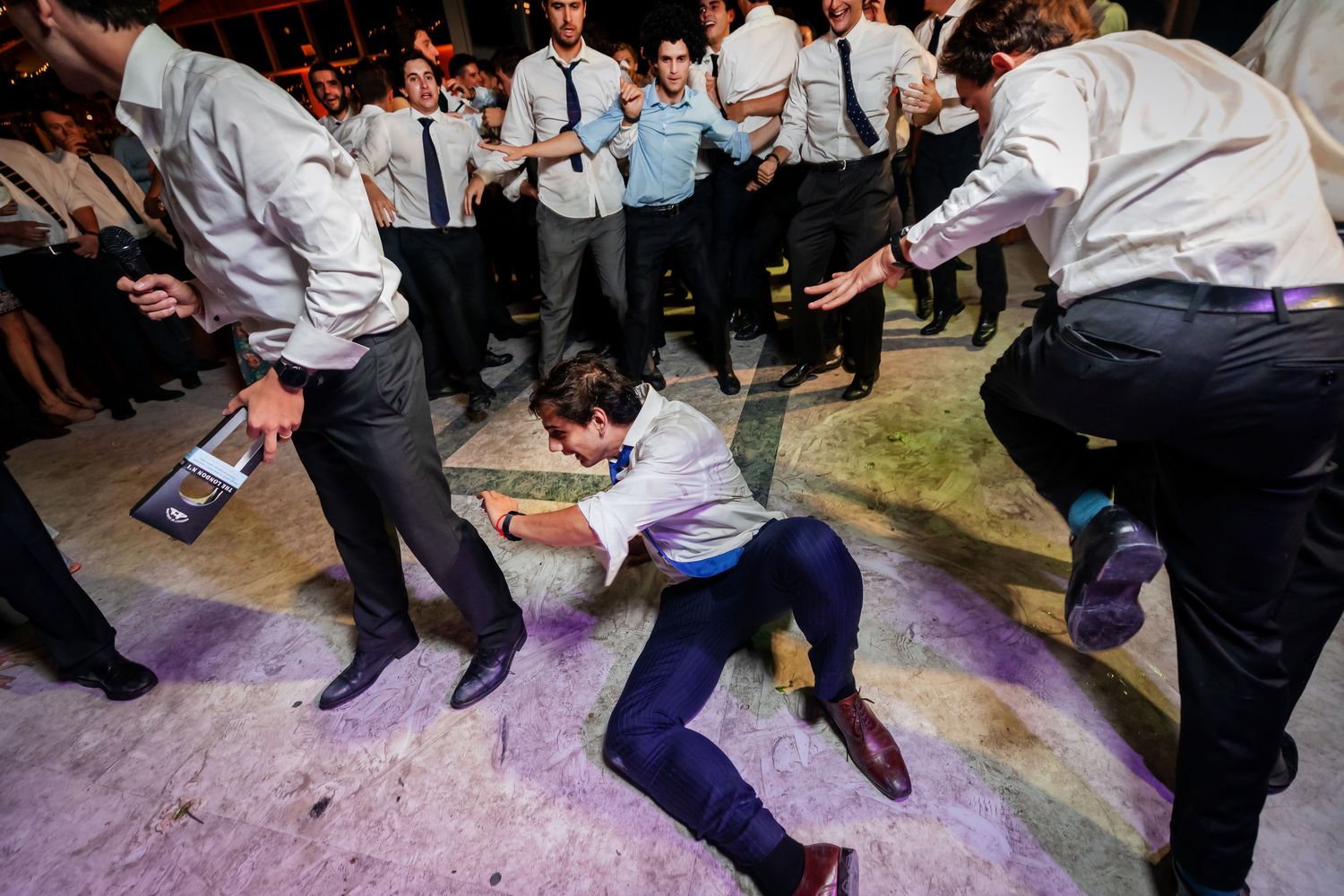 Groomsmen dancing energetically on the wedding reception dance floor, with one man doing a low move.