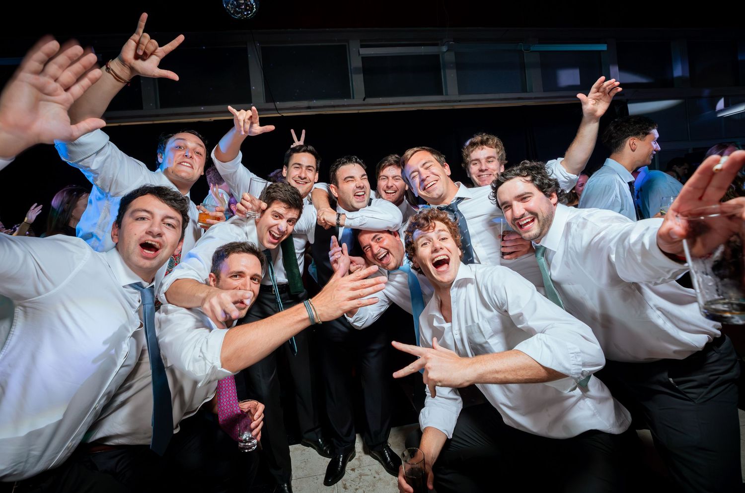 Group of male wedding guests posing together and celebrating on the dance floor at a wedding reception.