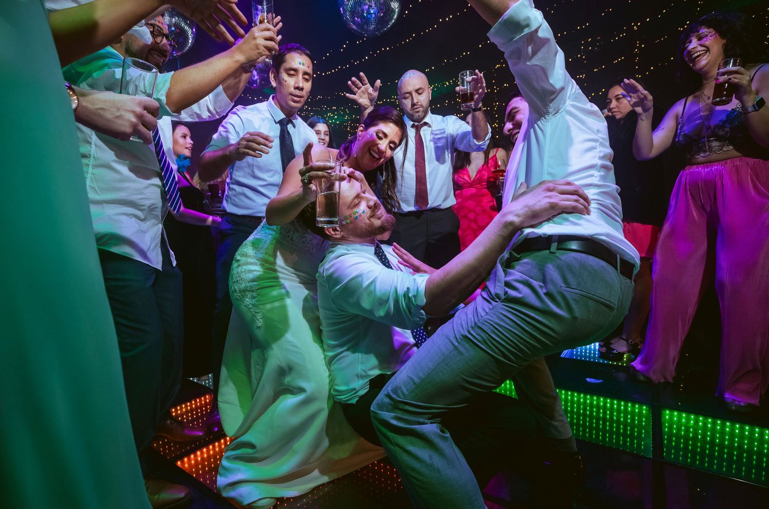 Guests dancing energetically on a lit dance floor at a lively wedding reception party.