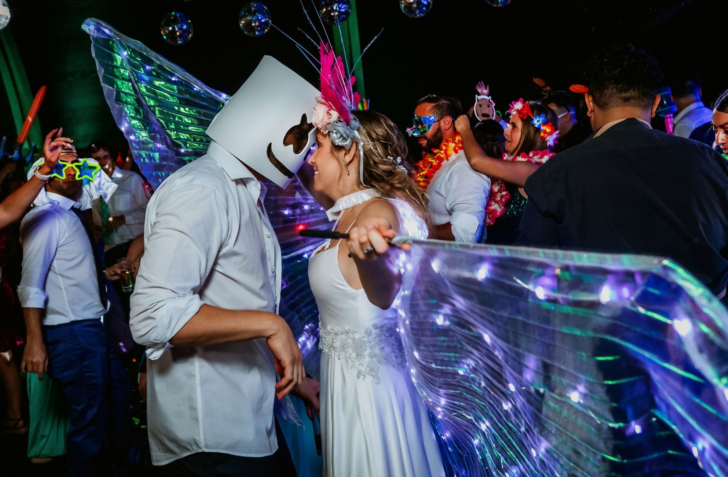 Couple sharing romantic kiss in glowing butterfly wings at wedding celebration.