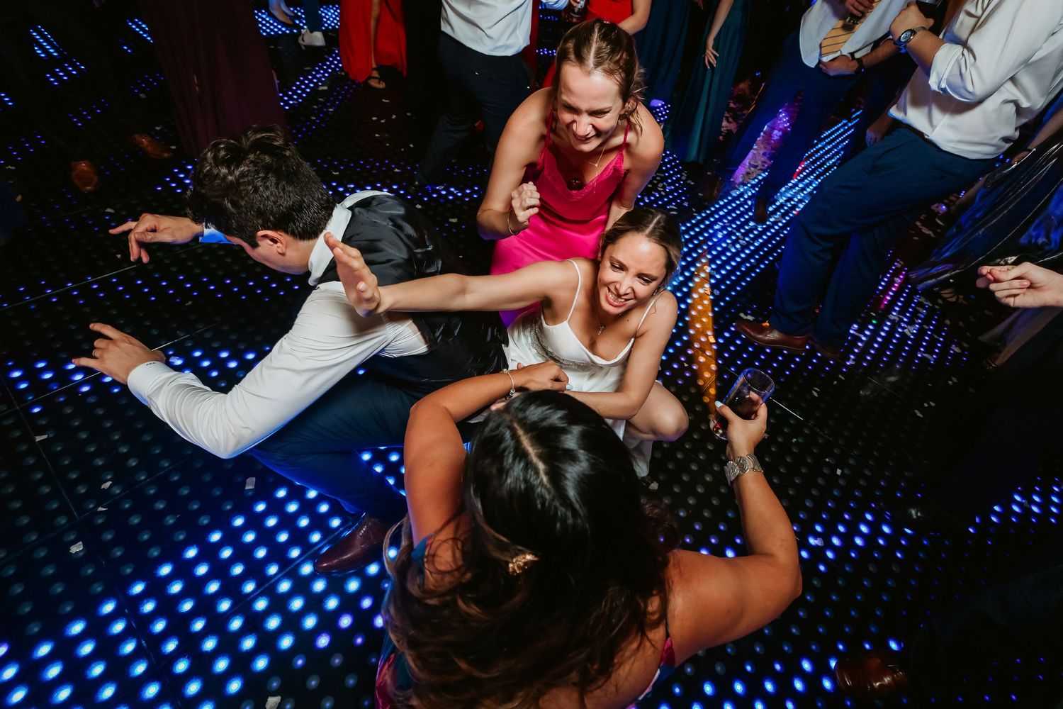 Guests dancing energetically on a lit dance floor at a lively wedding reception party.