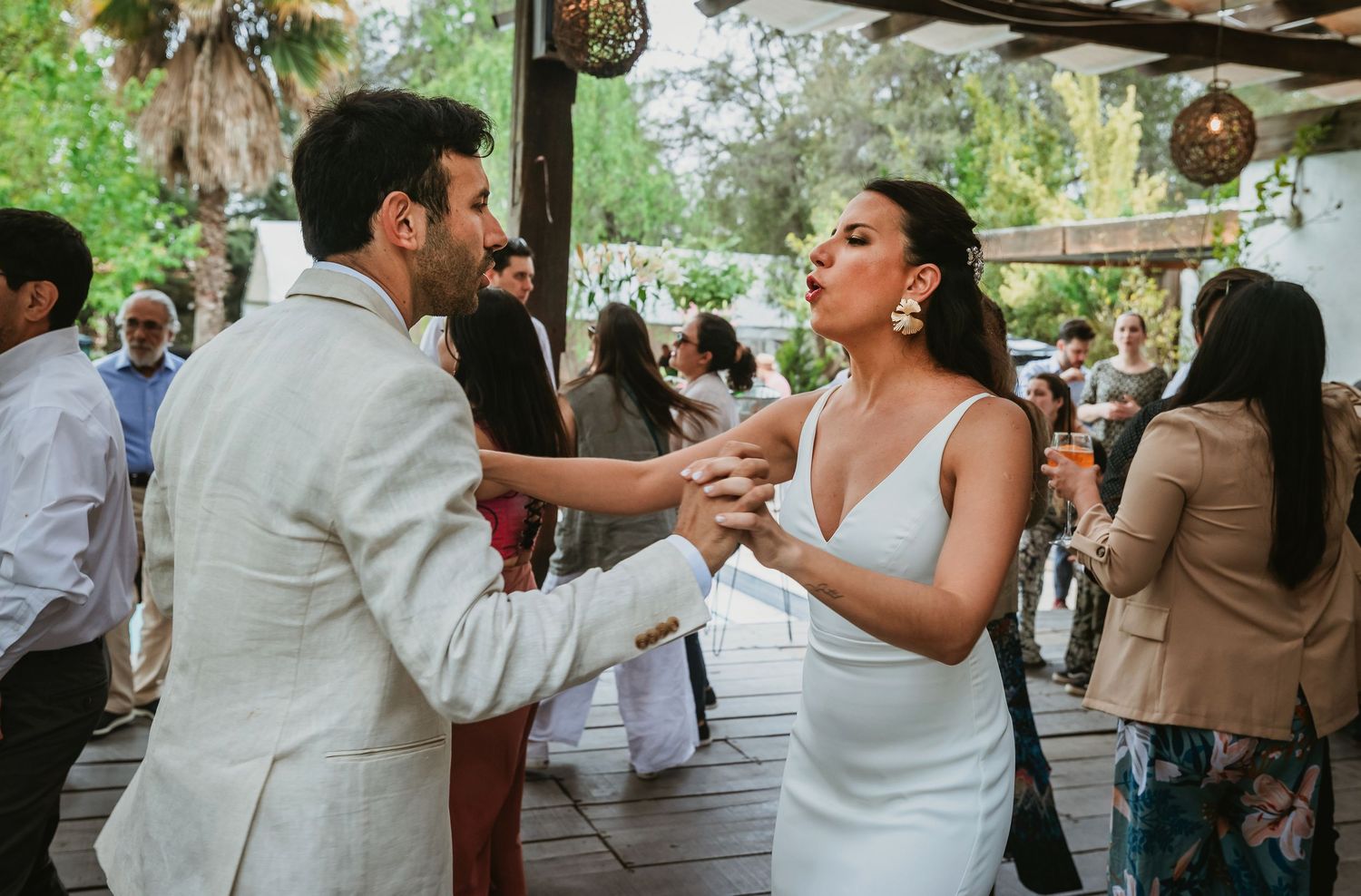 Bride and groom share first dance at outdoor wedding reception, bride in white gown, groom in ivory suit.