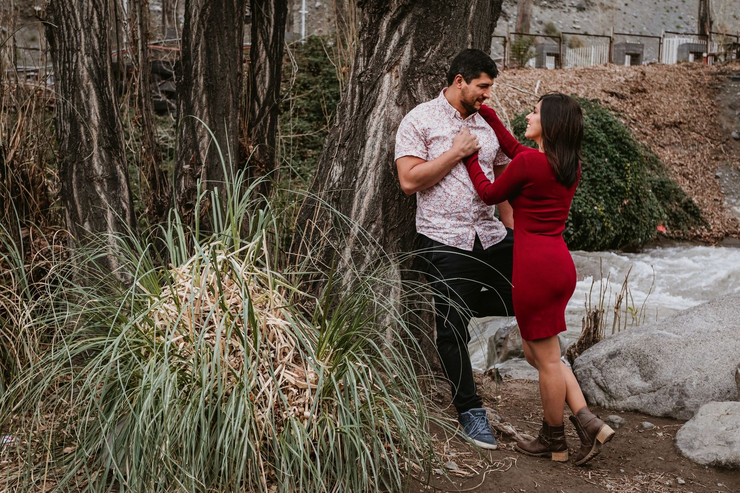 Playful couple dancing together near bare winter trees with snowy ground in romantic outdoor setting.