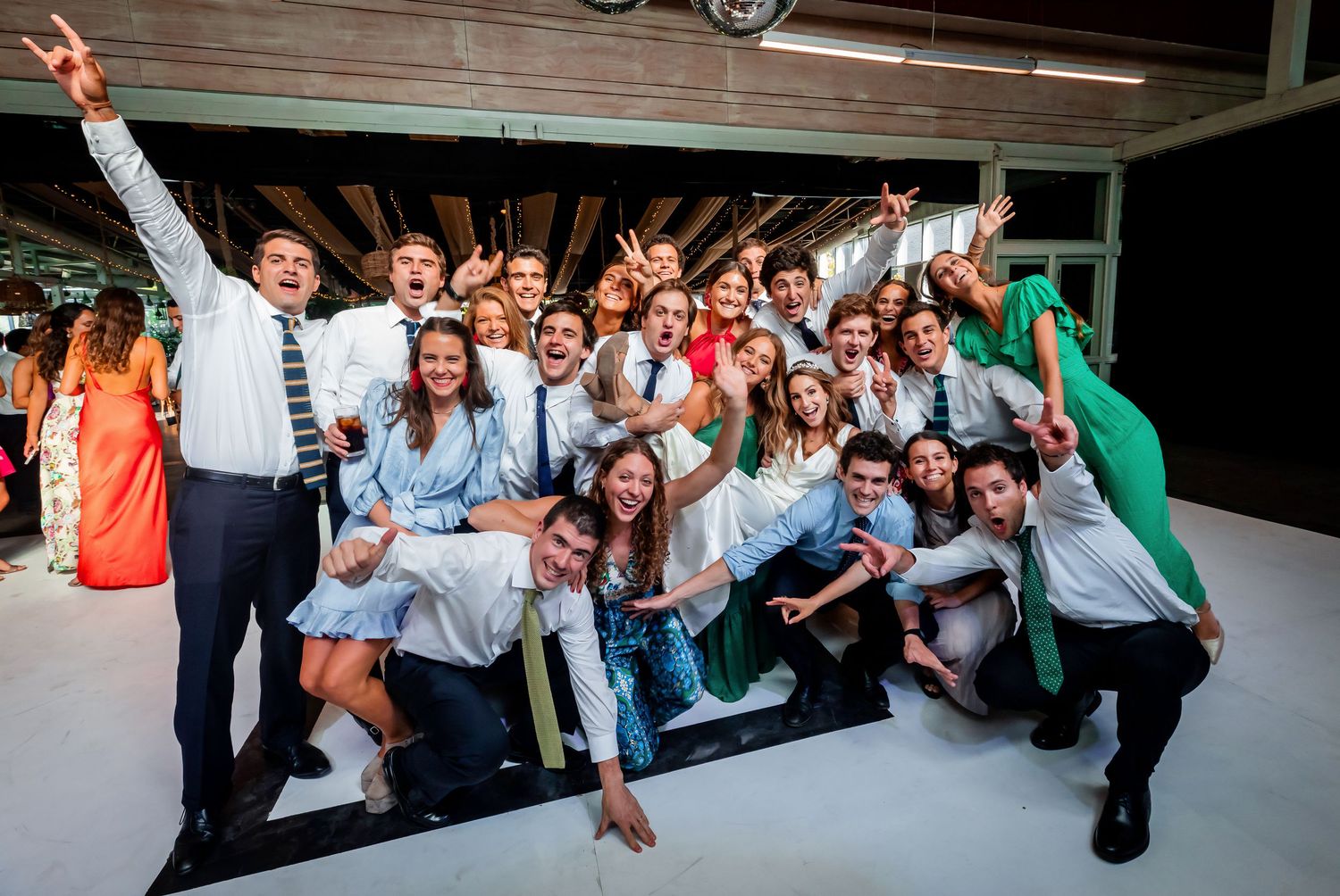 Large group of young wedding guests strike fun poses together on the dance floor.