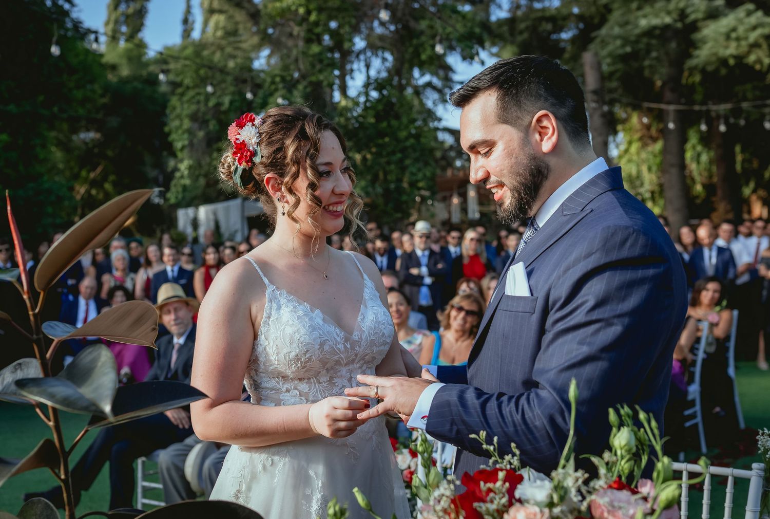 Bride and groom exchange rings and smile joyfully during outdoor garden wedding ceremony.