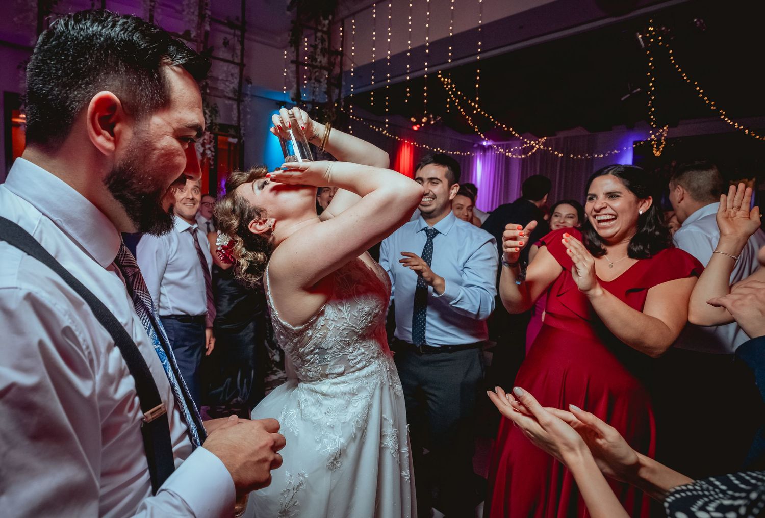 Bride celebrates joyfully on the dance floor with guests at lively wedding party reception.