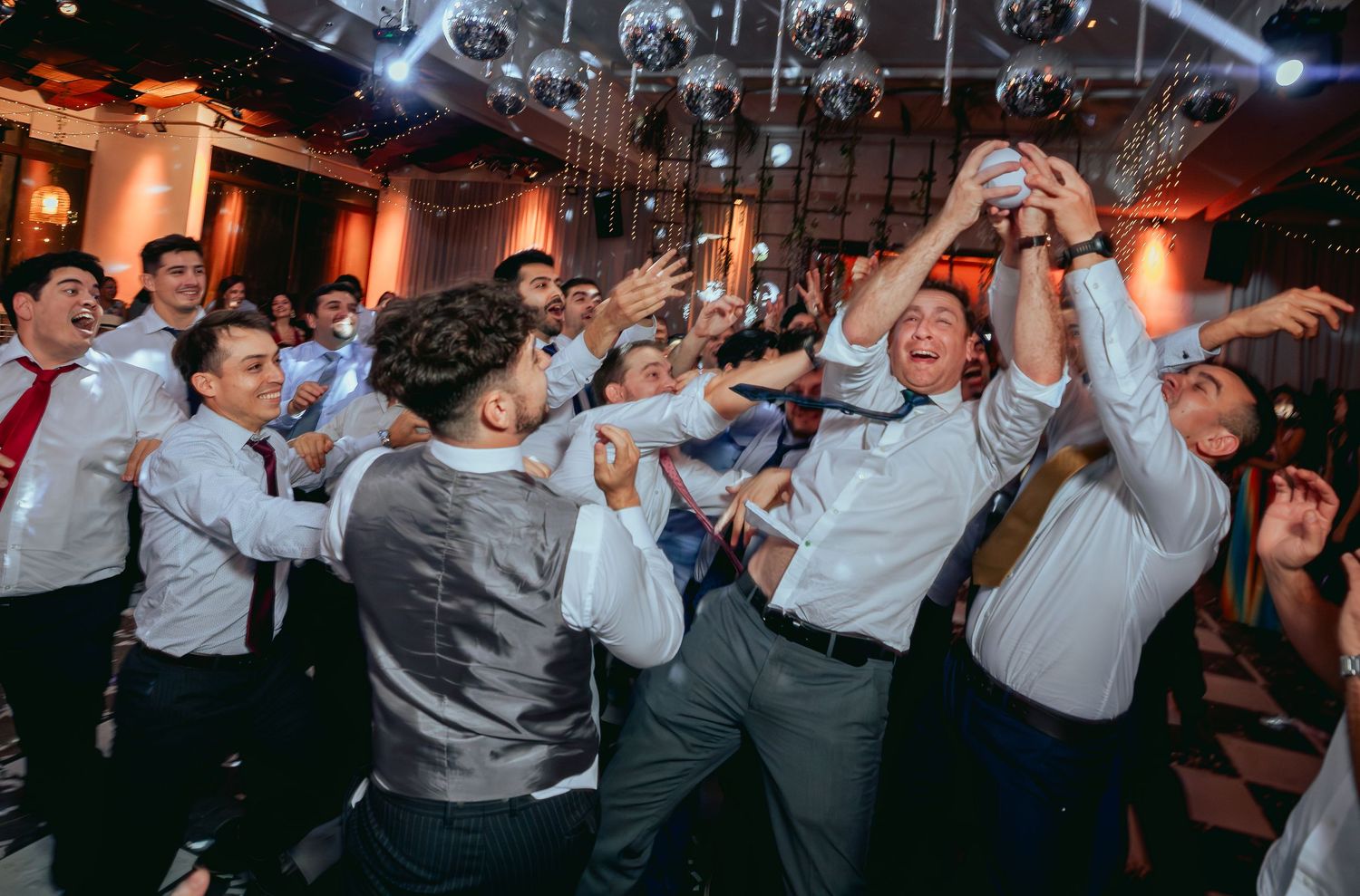 Excited wedding guests reaching and jumping together on crowded dance floor.