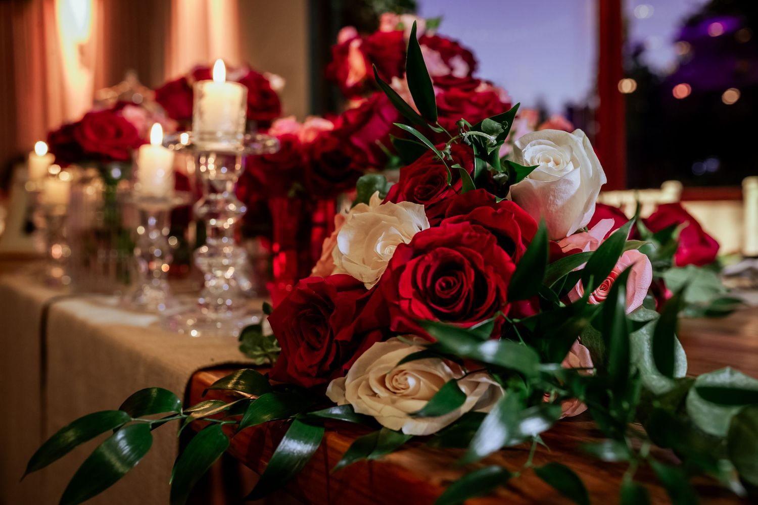 Stunning wedding centerpiece featuring red and white roses with candles at twilight.