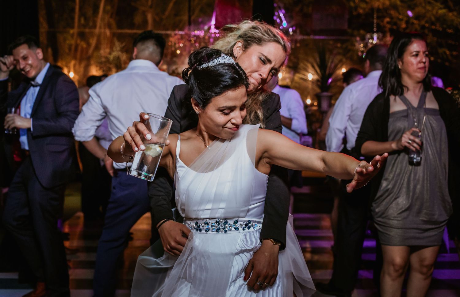 Bride in white dress dancing joyfully with a guest at an outdoor wedding reception.