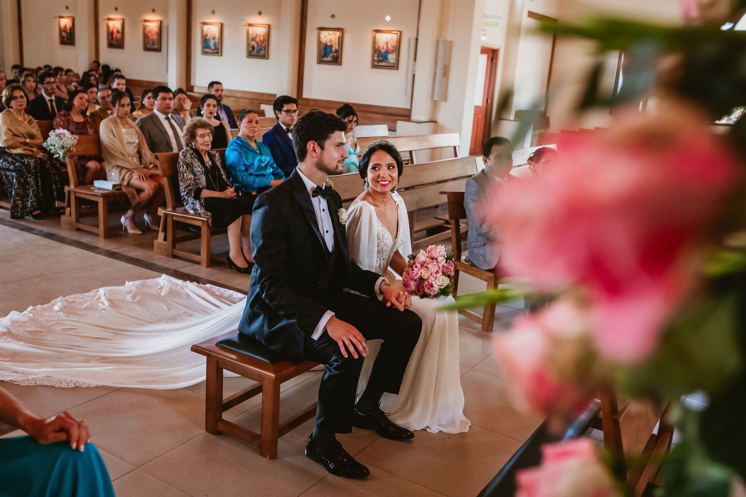 Bride and groom seated together during church wedding ceremony surrounded by guests in pews.