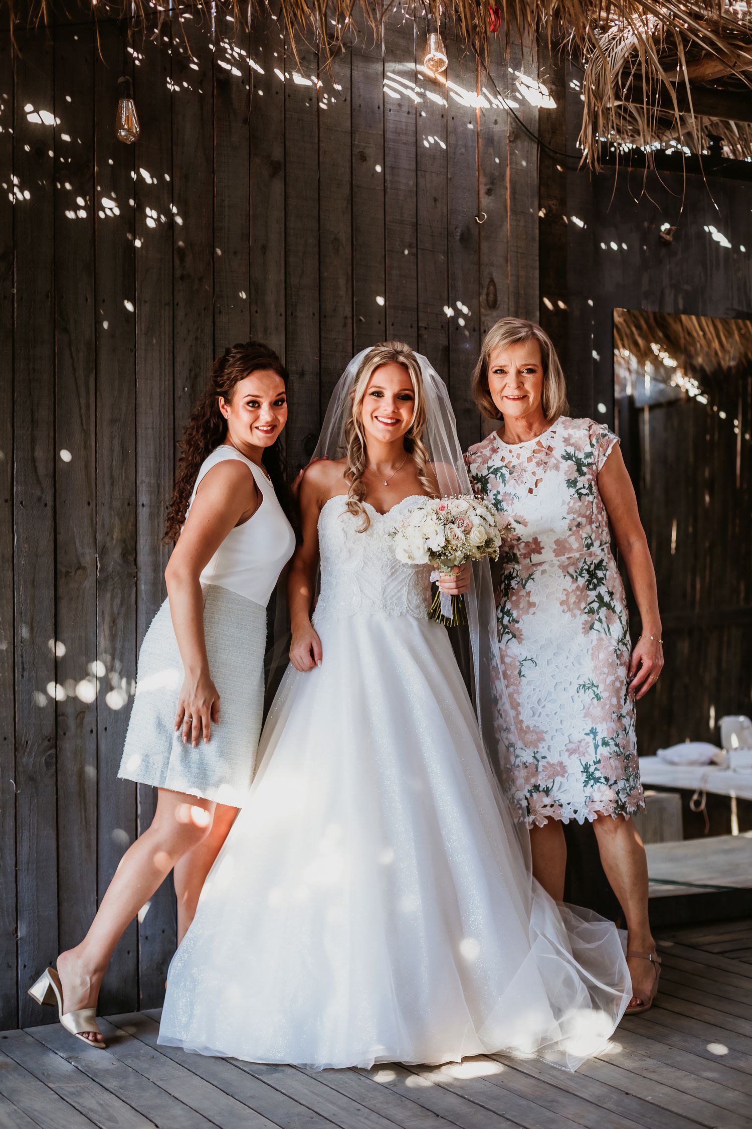 Bride in white ball gown posing with bridesmaid and mother in floral dress at barn wedding.