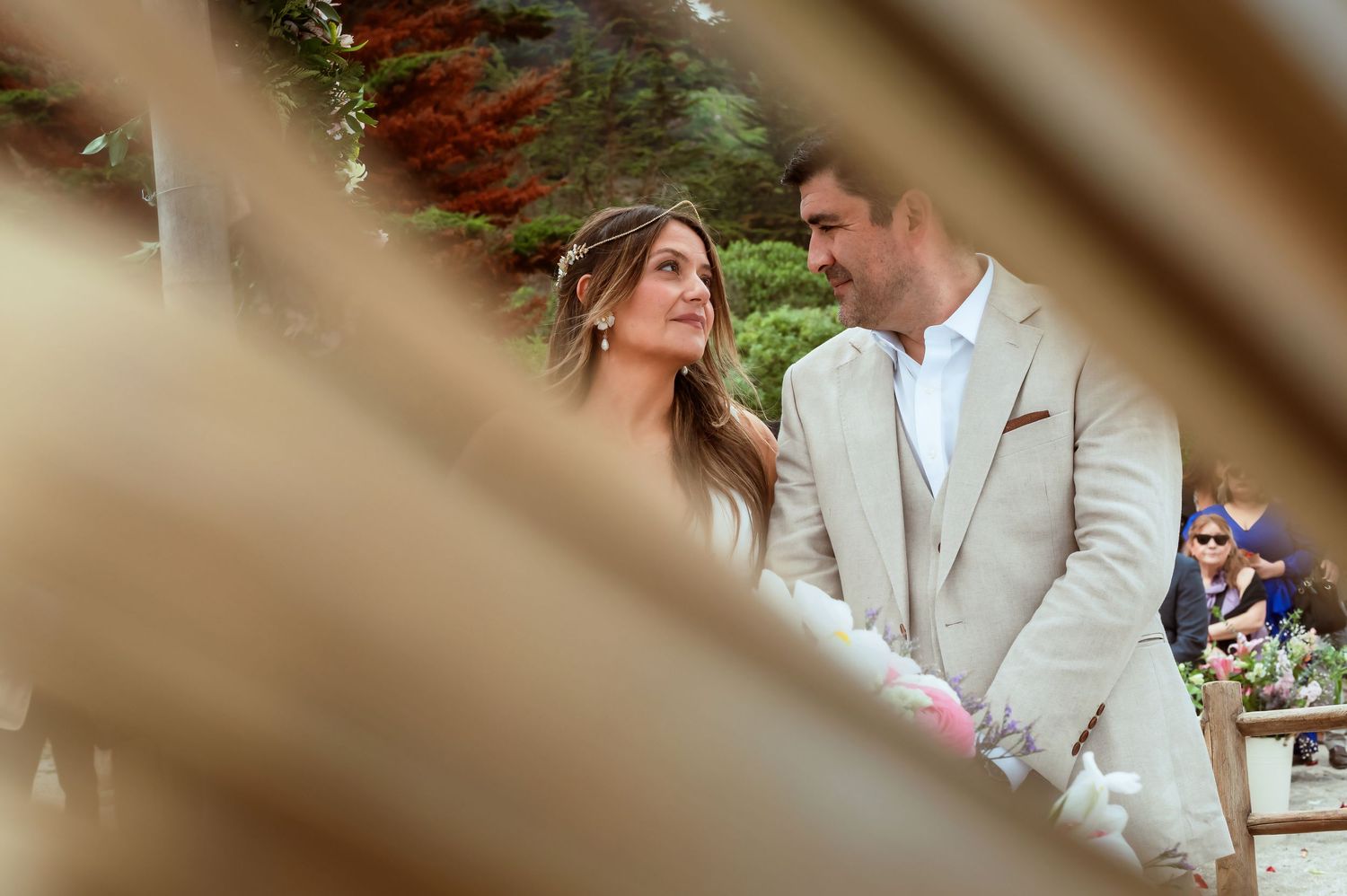 Bride and groom share an intimate glance during outdoor wedding ceremony framed by wooden decor.