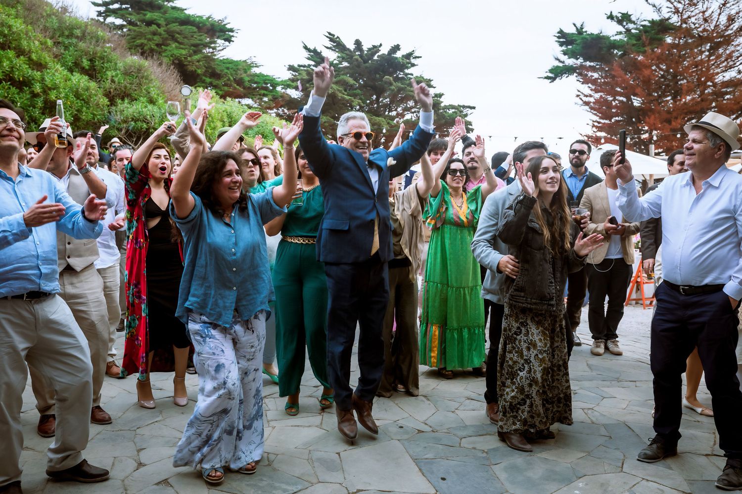 Joyful wedding guests dancing together at an outdoor coastal garden celebration.