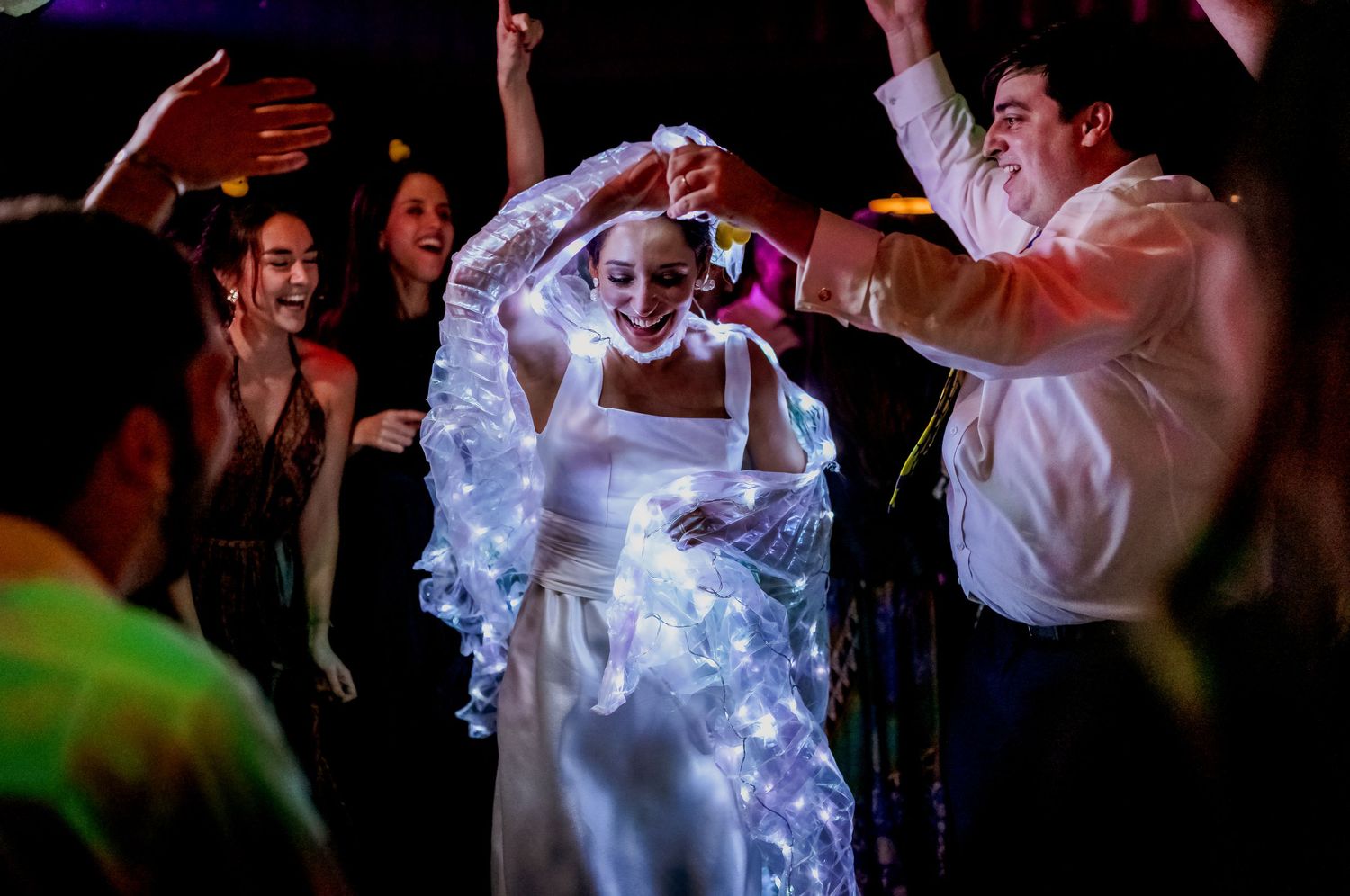 Bride in white gown and veil dancing joyfully with guests at a lively wedding reception party.