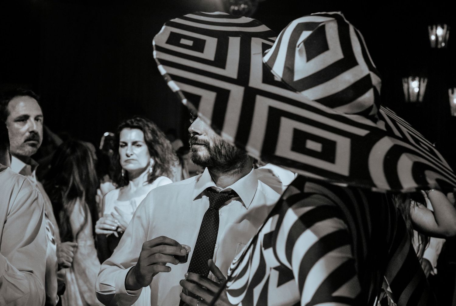 Black and white photo of wedding guests with performer in bold optical illusion black and white costume and hat.