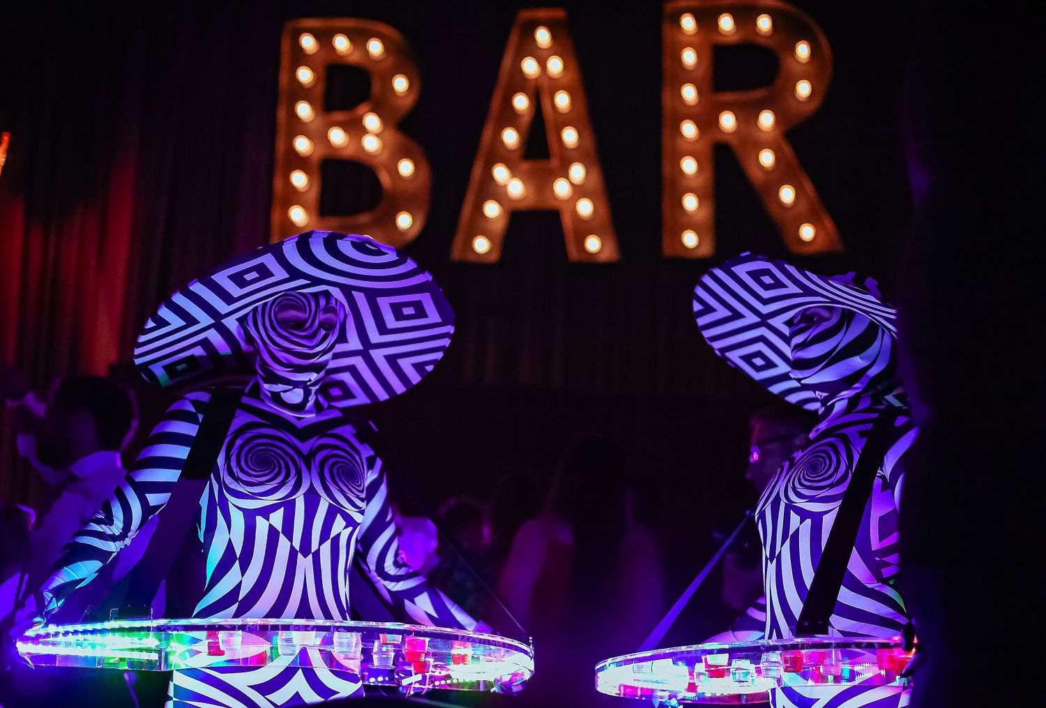 Two performers in illuminated zebra-print costumes pose under a lit BAR sign at a nightclub.