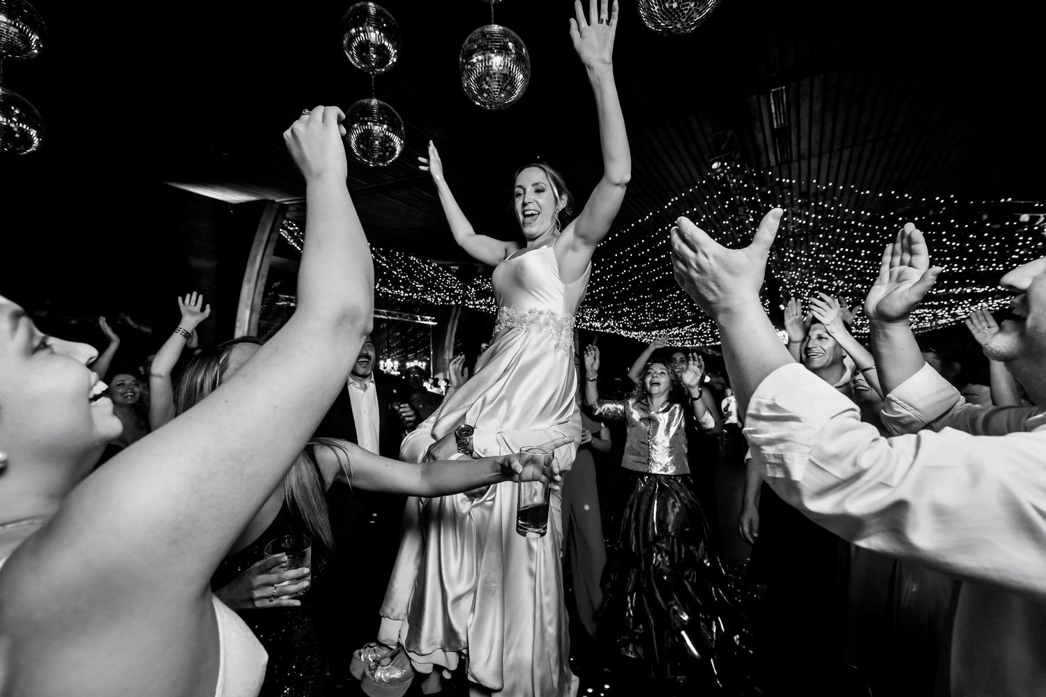 Bride lifted by guests on wedding dance floor in black and white photo.