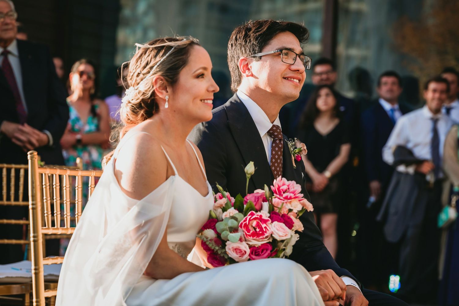 Happy bride and groom share a joyful moment seated during their outdoor wedding ceremony.