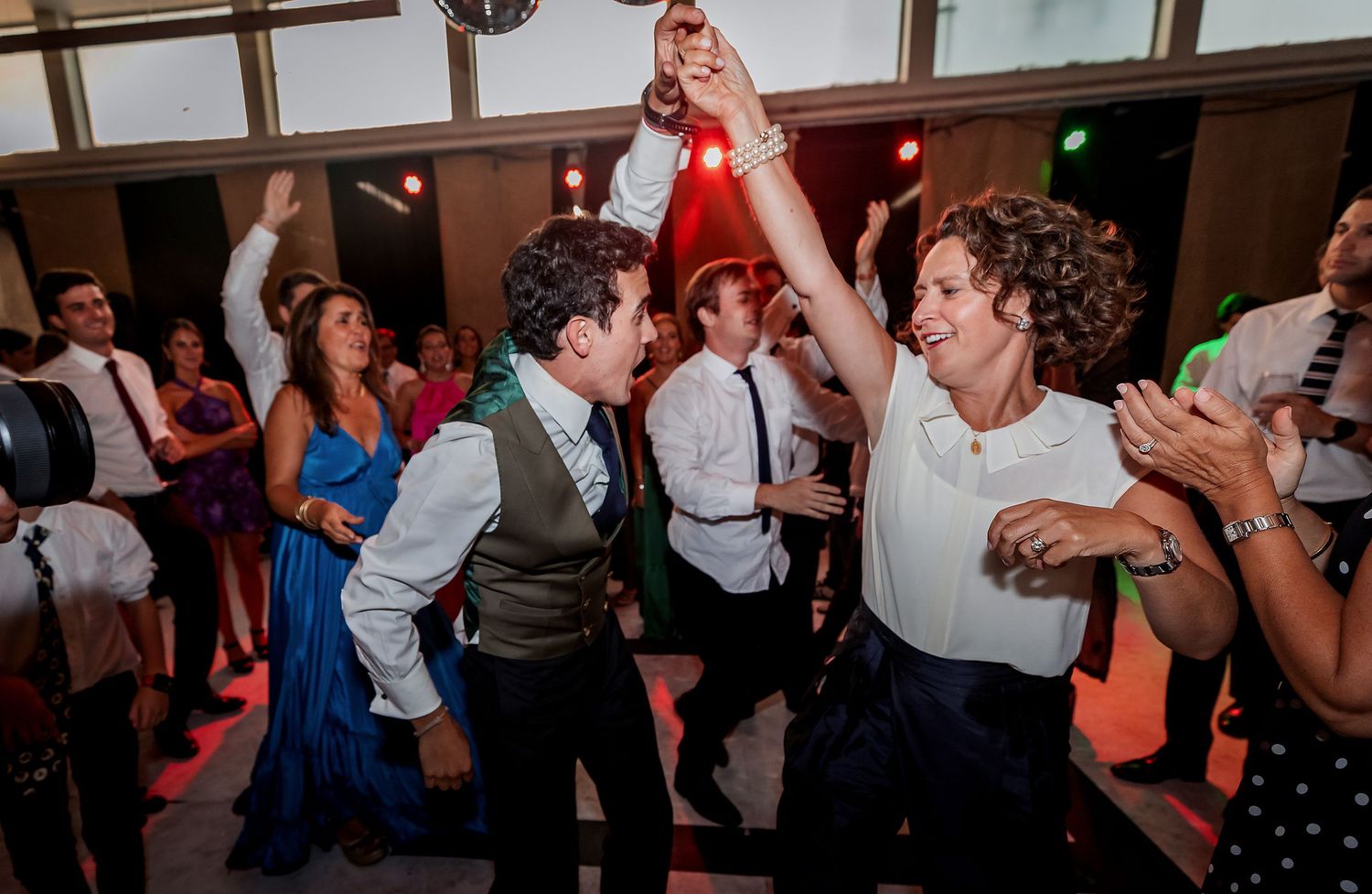 Bride and female guest dancing together holding hands at a vibrant wedding reception party.