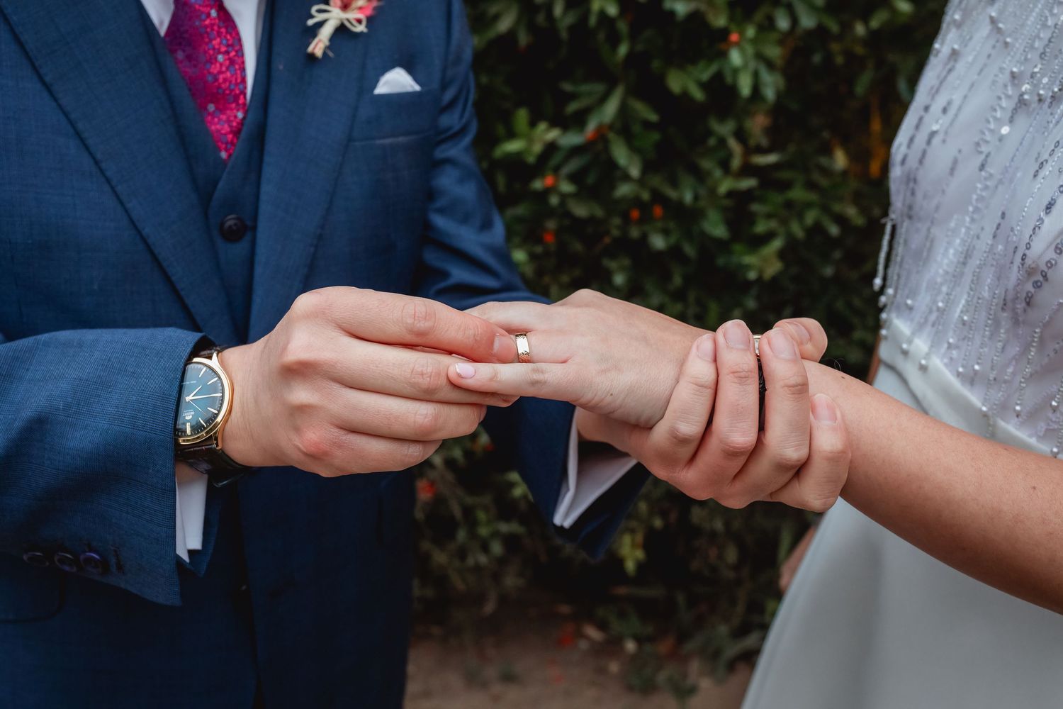 Groom places wedding ring on brides finger during outdoor wedding ceremony ring exchange.
