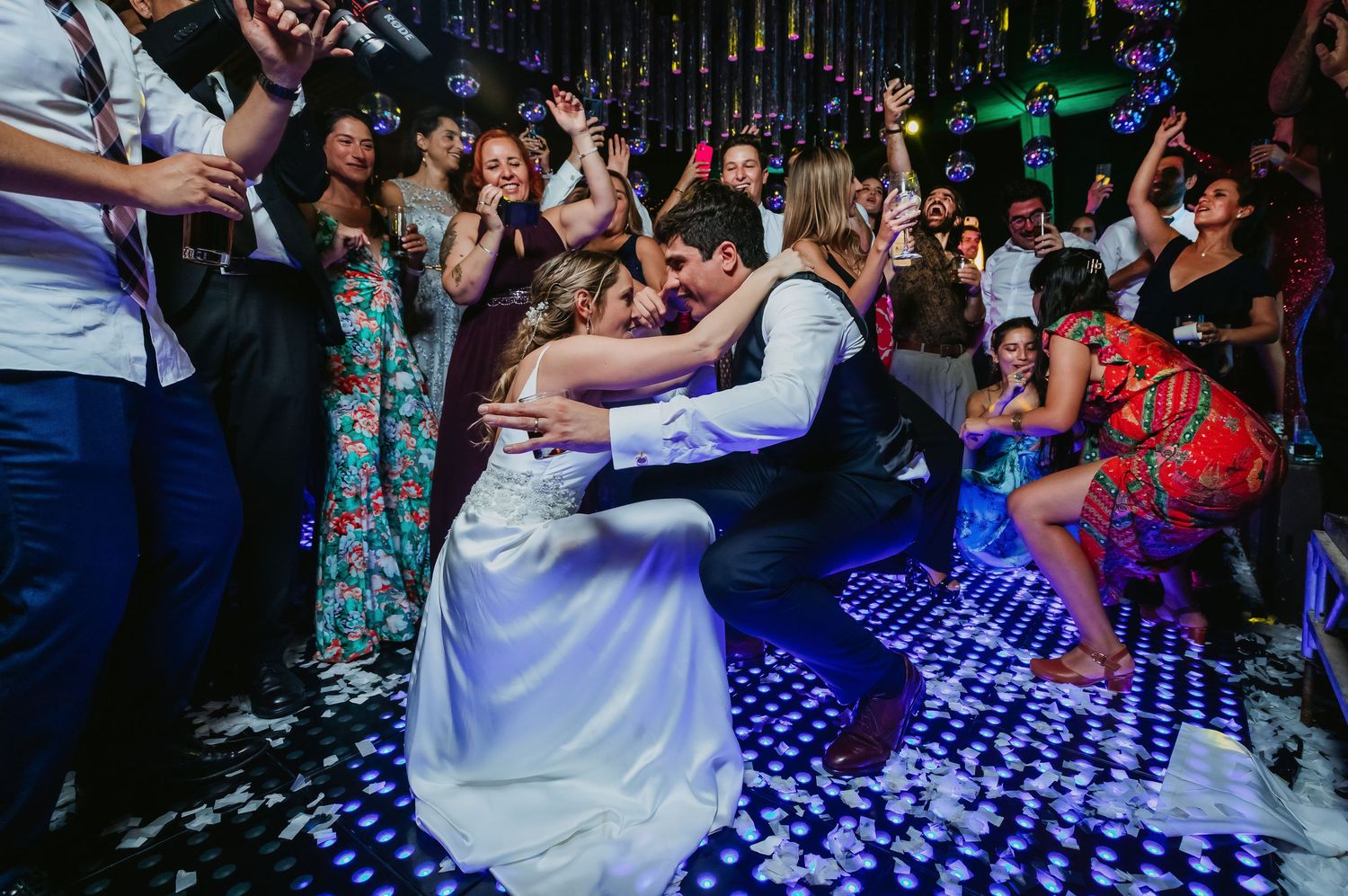 A bride and groom share a romantic dip on a sparkling dance floor surrounded by celebrating wedding guests.