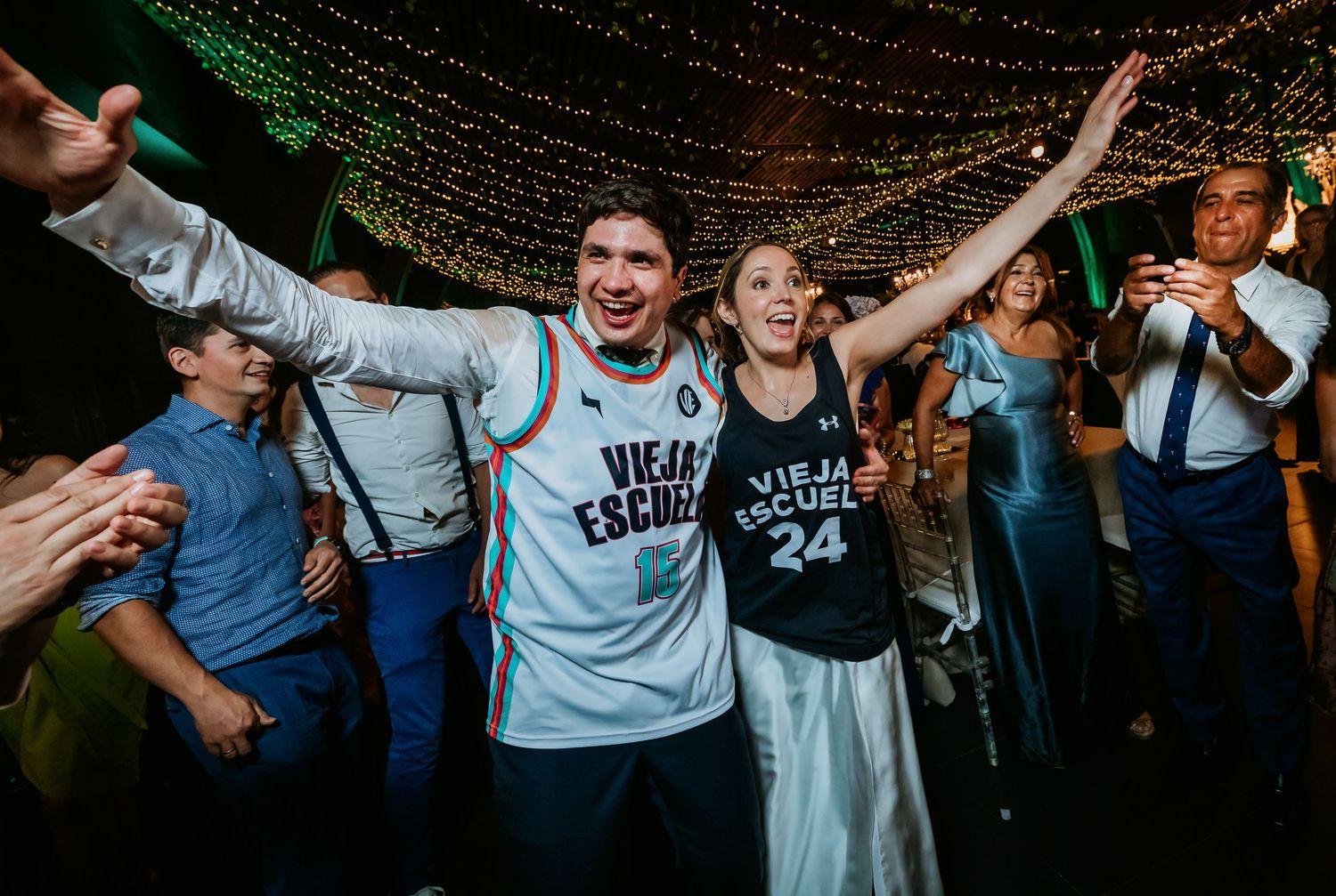 Excited couple in matching Vieja Escuela jerseys celebrating on a wedding dance floor.