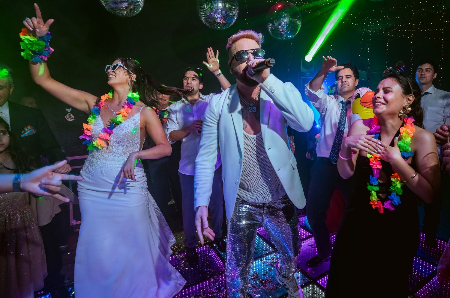 Lively nightclub party with people dancing under disco balls and neon lights, wearing colorful Hawaiian leis.
