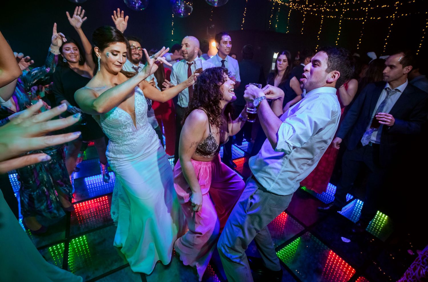 Wedding guests dancing energetically on a colorful LED dance floor at a lively reception party.