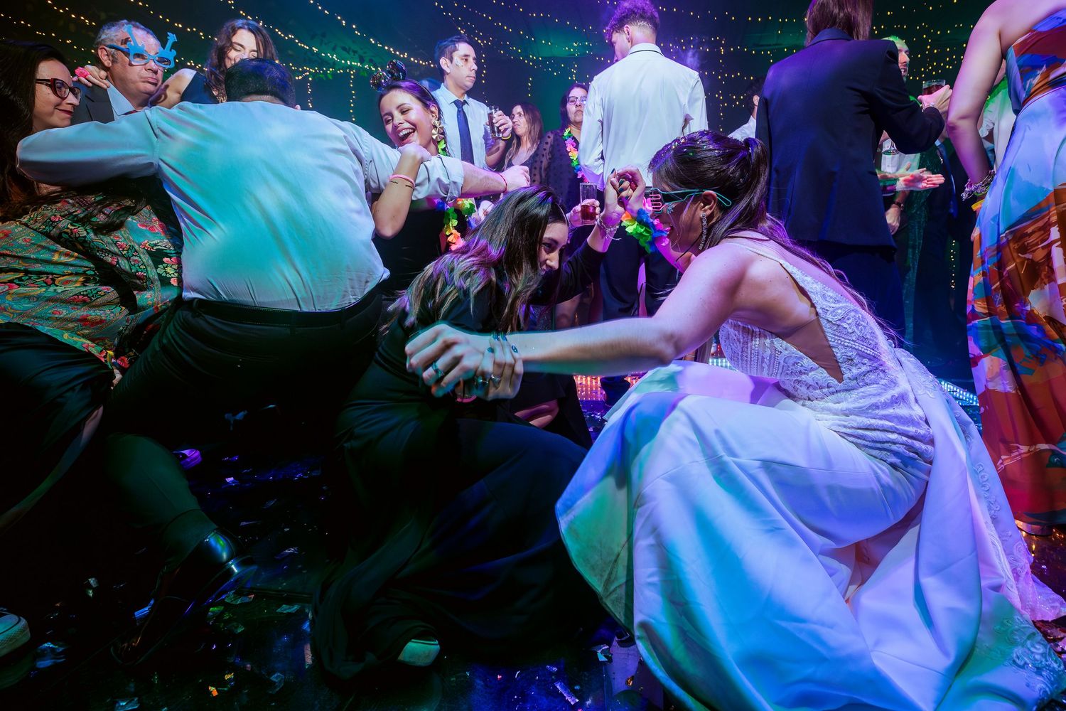 Guests in formal attire dancing energetically on a confetti-filled wedding reception dance floor at night.