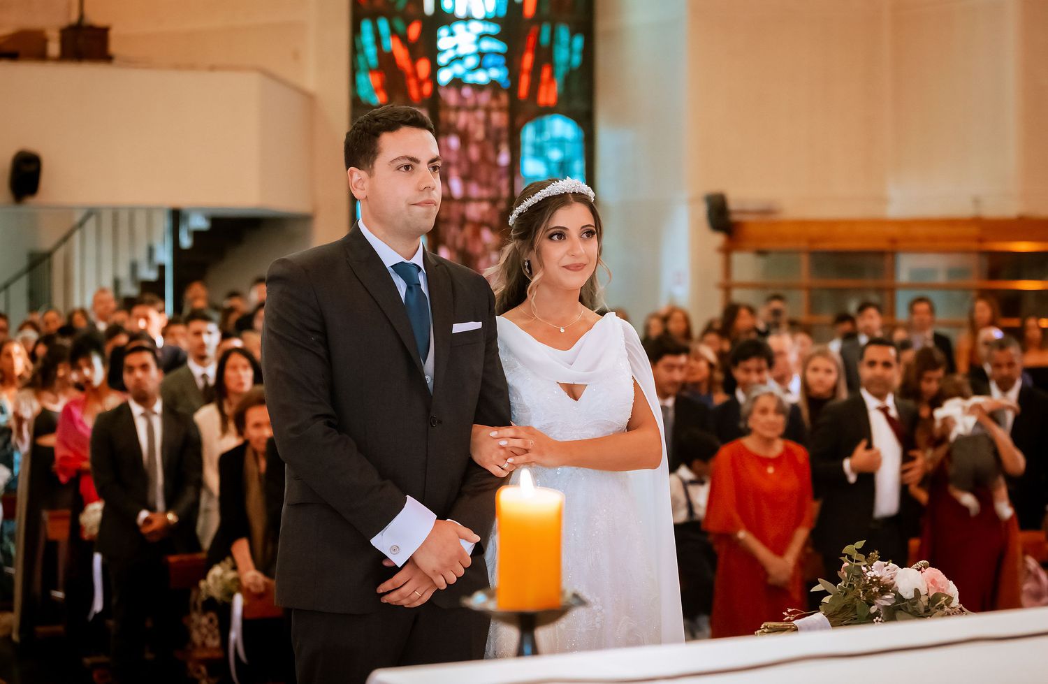 Bride and groom standing together at church altar during wedding ceremony with guests seated behind them.