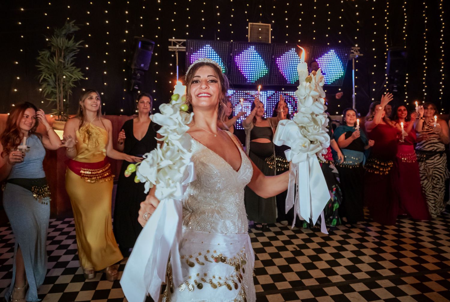 Bride in lace gown dancing with floral candles at a festive wedding reception.
