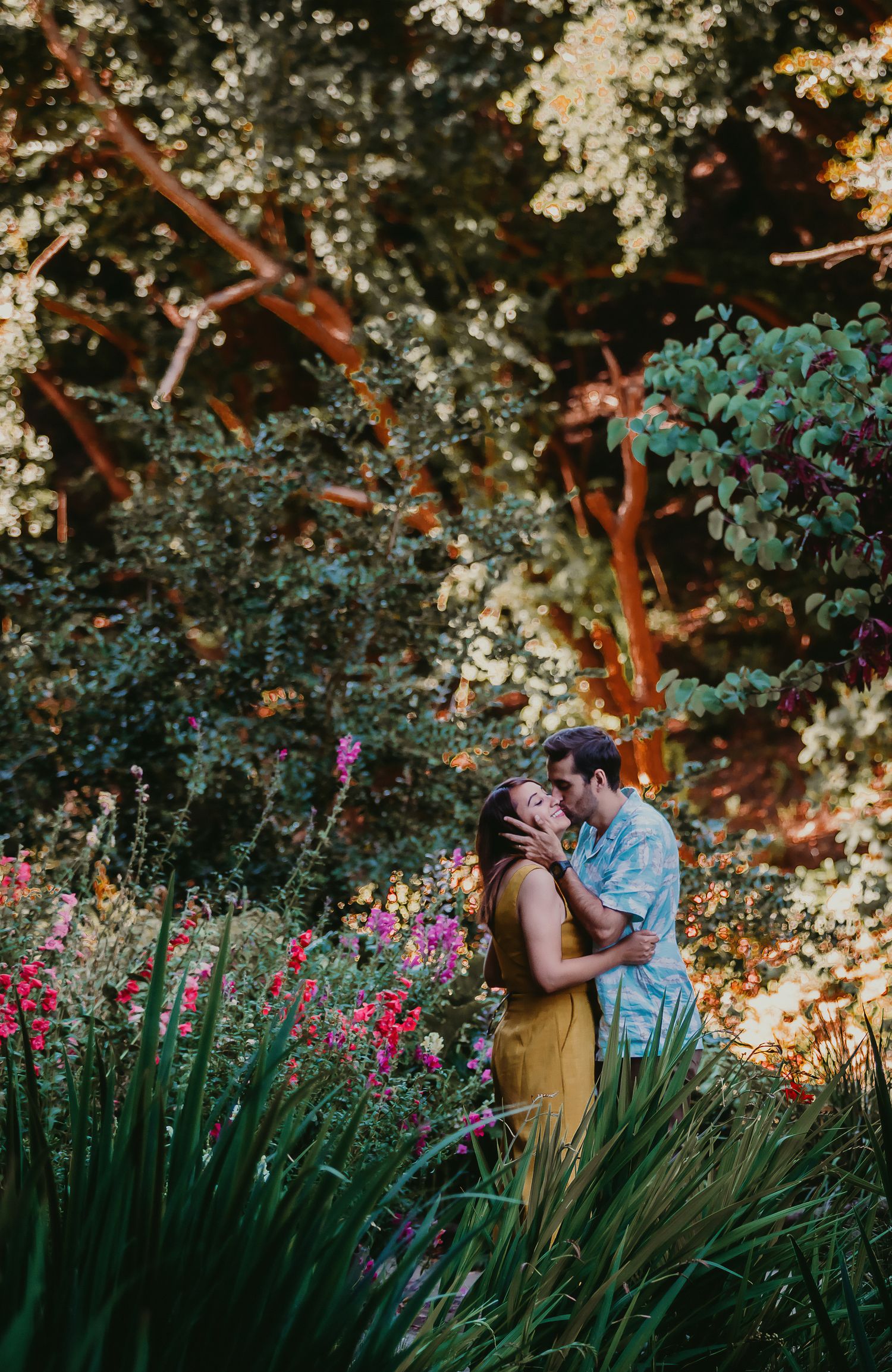 Romantic couple kissing in a vibrant garden filled with colorful flowers and glowing trees.