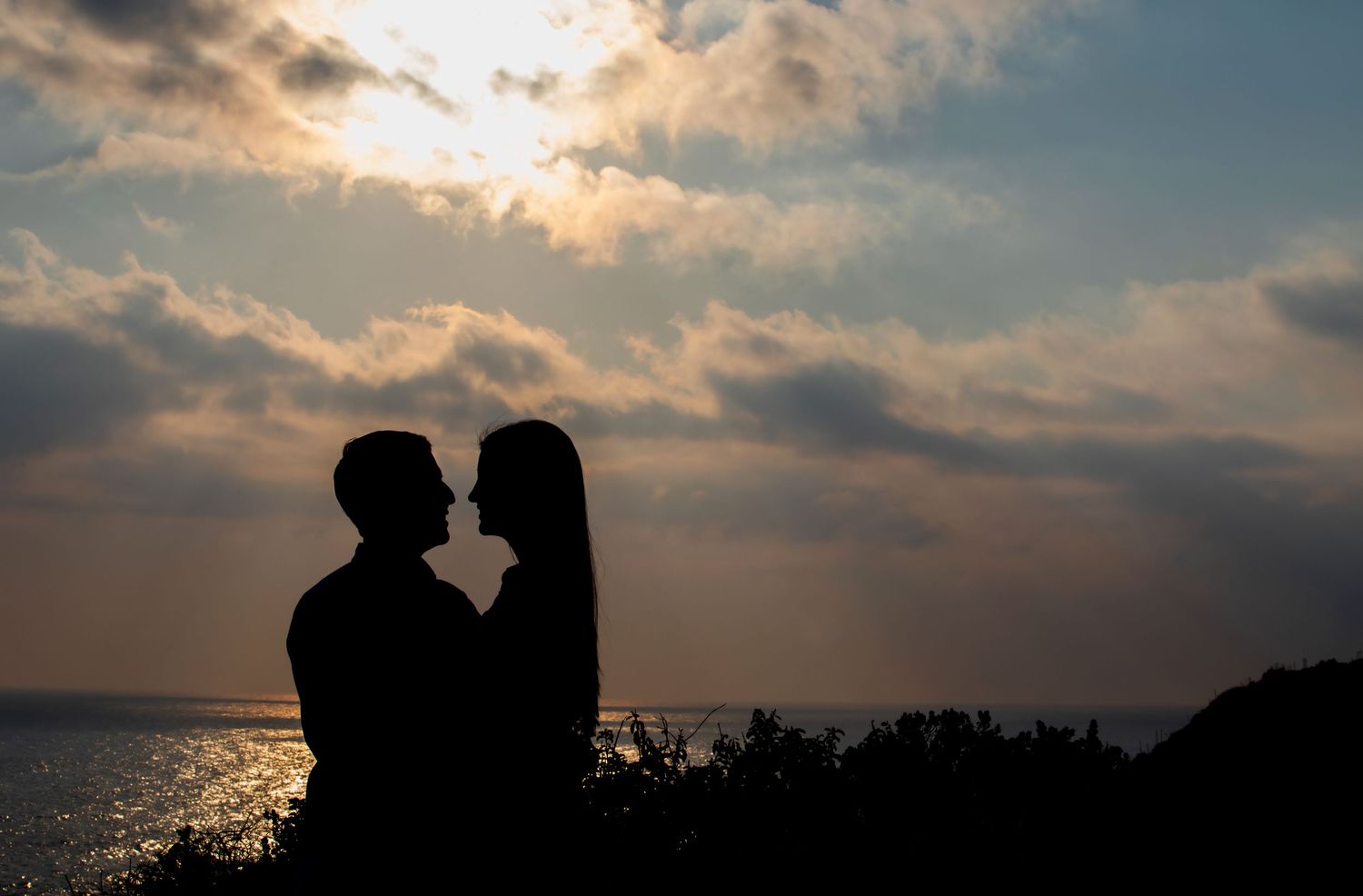 Silhouette of romantic couple about to kiss against dramatic sunset over ocean.