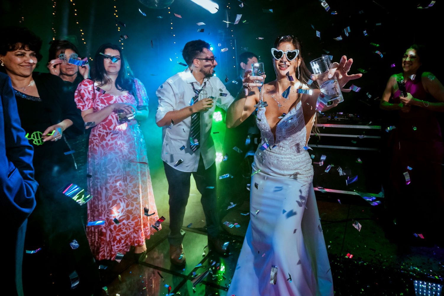 Bride in white gown celebrates with confetti and guests at a vibrant nightclub wedding reception.