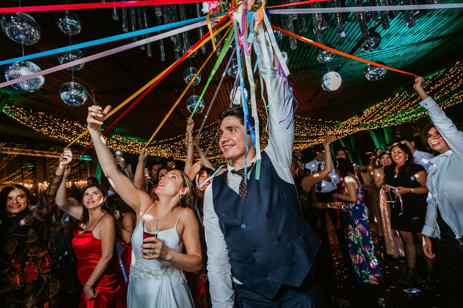 Bride and groom celebrating with colorful streamers under disco ball lights.