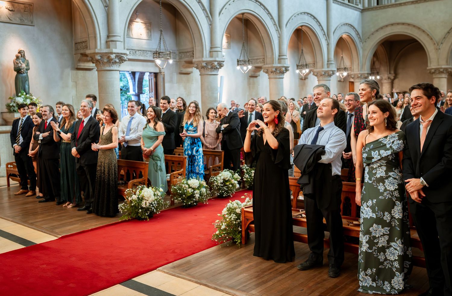 Wedding guests standing and singing together inside grand church with red carpet aisle.
