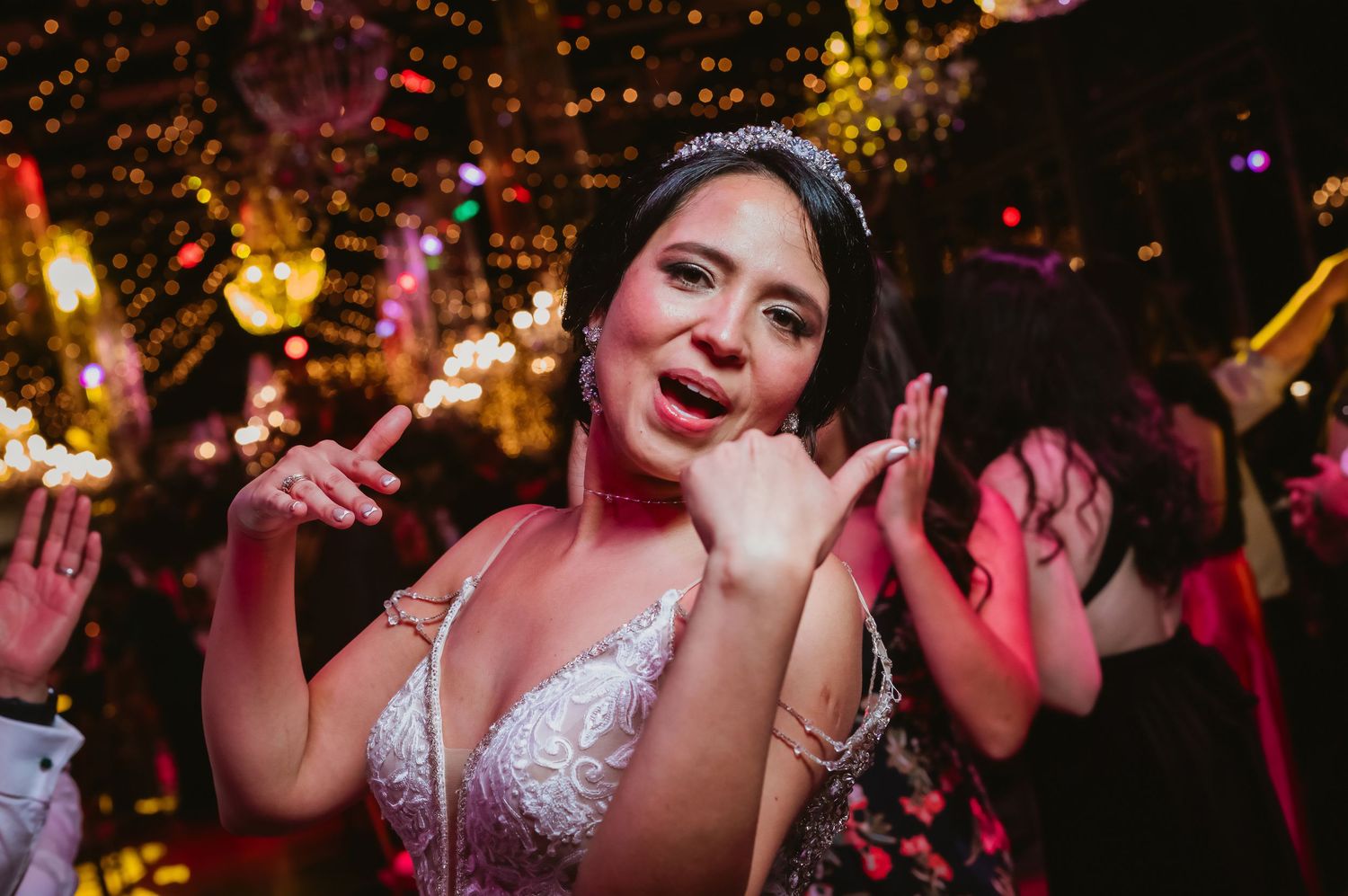 Bride in white lace gown wearing a tiara smiling joyfully at her wedding reception.